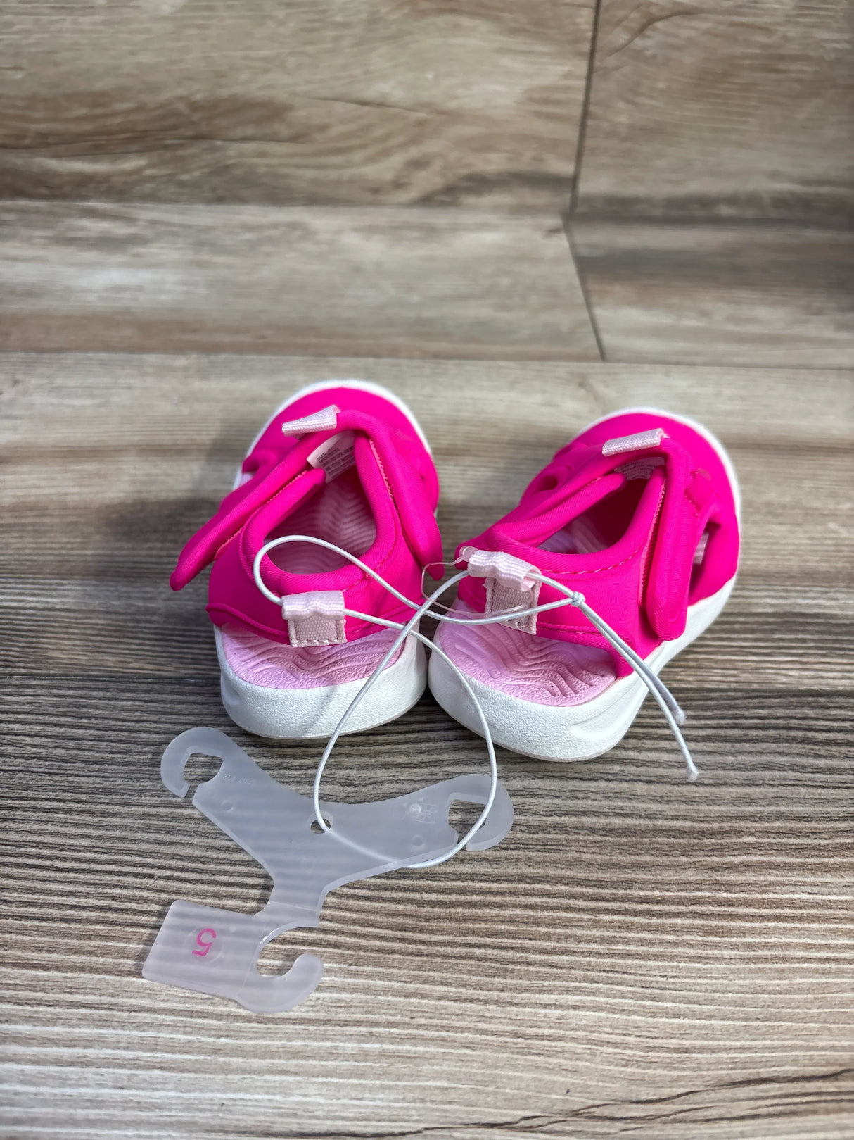 Rear view of Cat & Jack toddler water shoes, bright pink with white soles, velcro straps and textured insoles on a wood-grain backdrop
