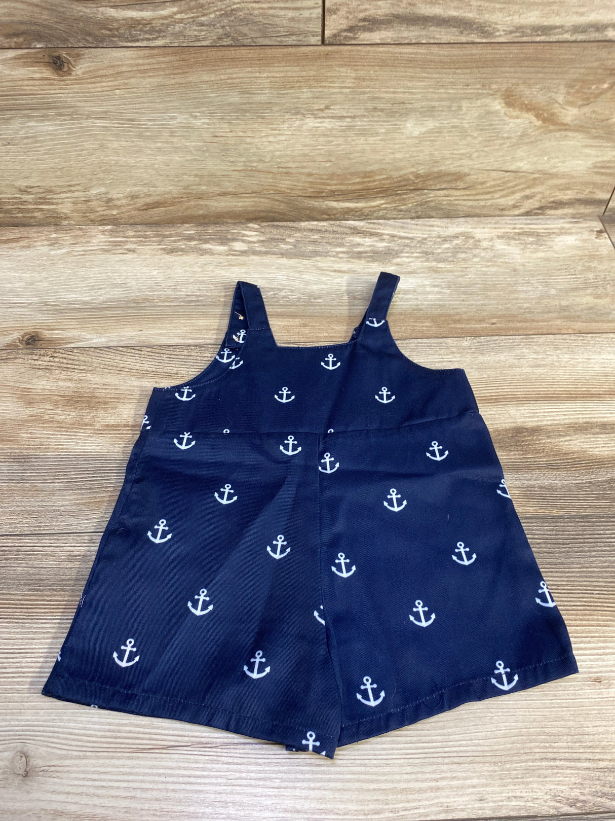 Front view of navy anchor-print shortalls showcasing thin shoulder straps and stitched waist seam on light wood background