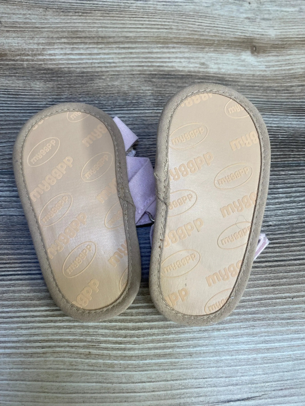 Bottom view of toddler cross-strap pearl sandals (size 5/6C) showing branded soles and pink straps on wood surface