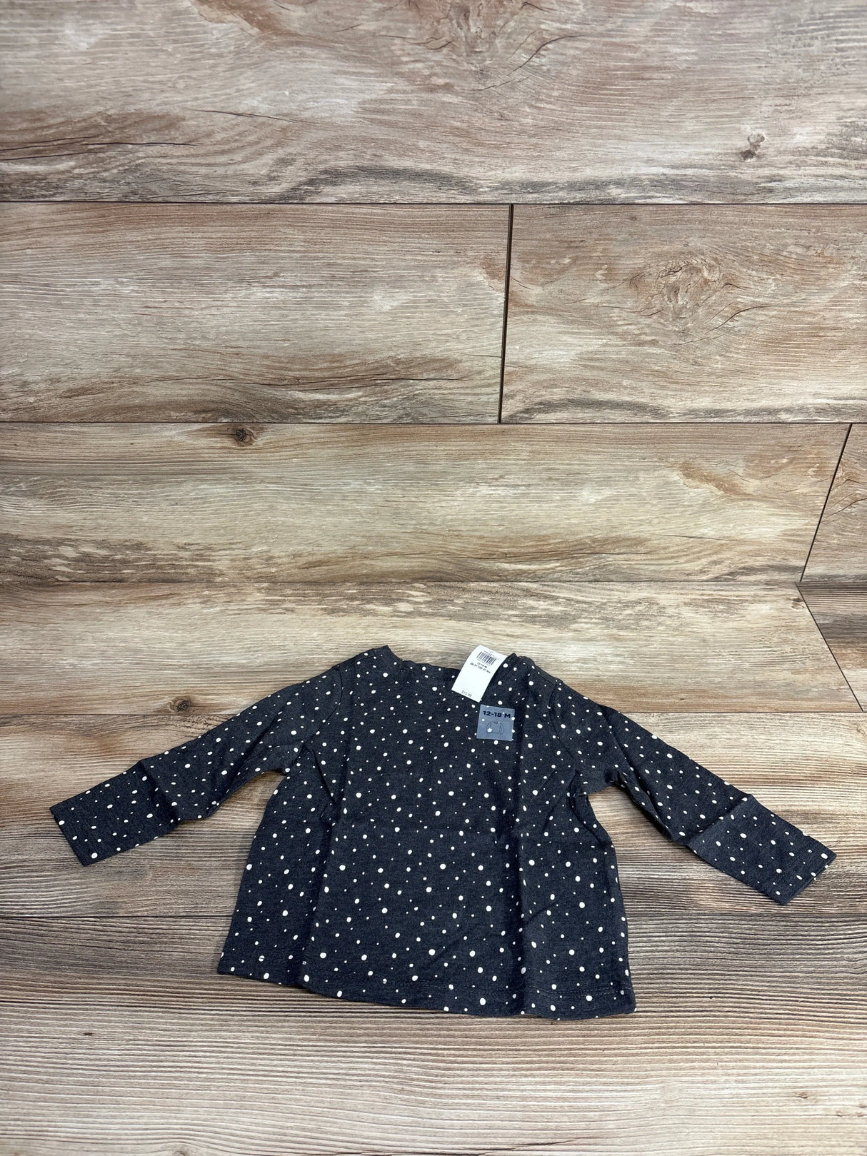 Flat lay of Old Navy long-sleeve grey toddler shirt (12-18M) showcasing white polka dot print and retail tag on wood plank background