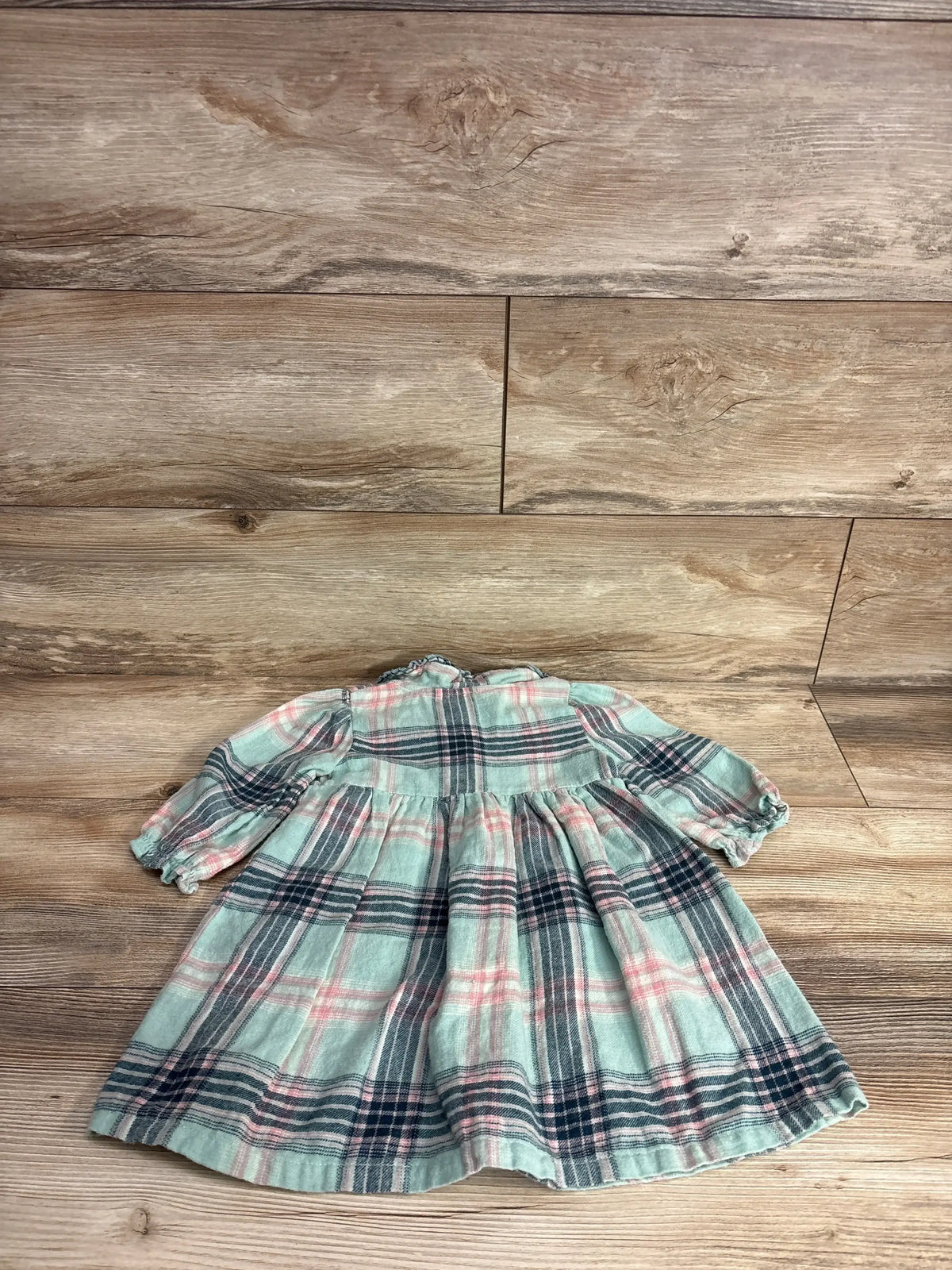 Plaid long sleeve toddler dress with pastel green, pink, and navy checks on wood background