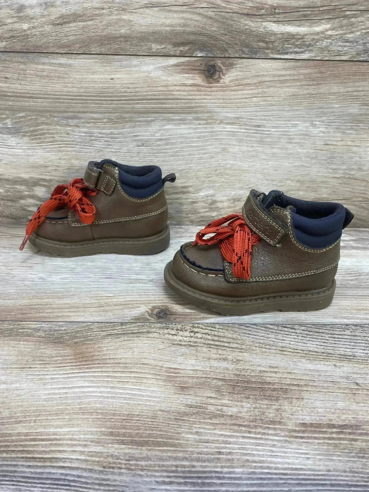 Side view of Carter’s toddler Norman brown ankle boots showing red laces, padded navy collar and stitched sole on wood background