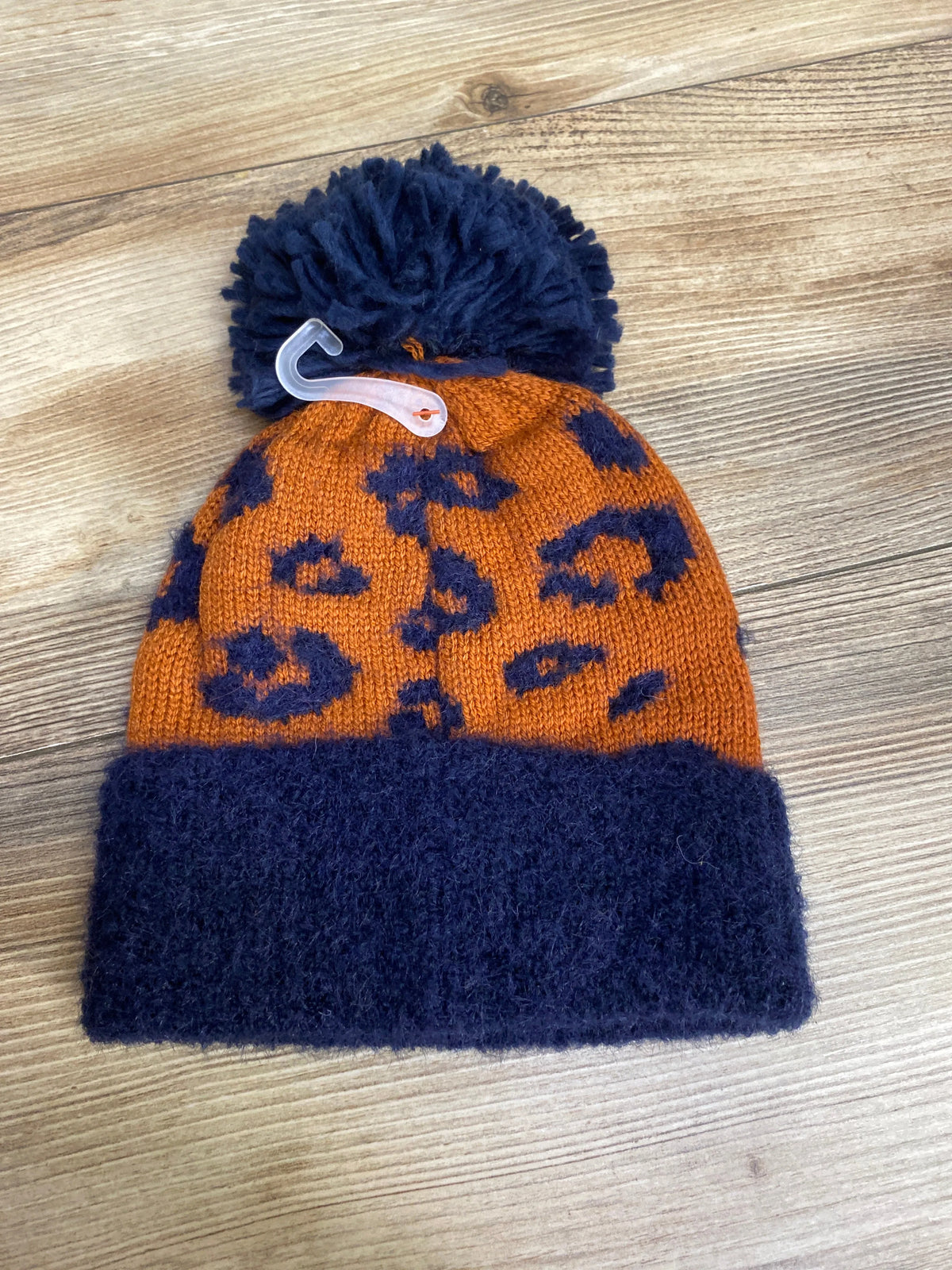 Orange and navy blue knit winter beanie with leopard print pattern and pom-pom on wood surface