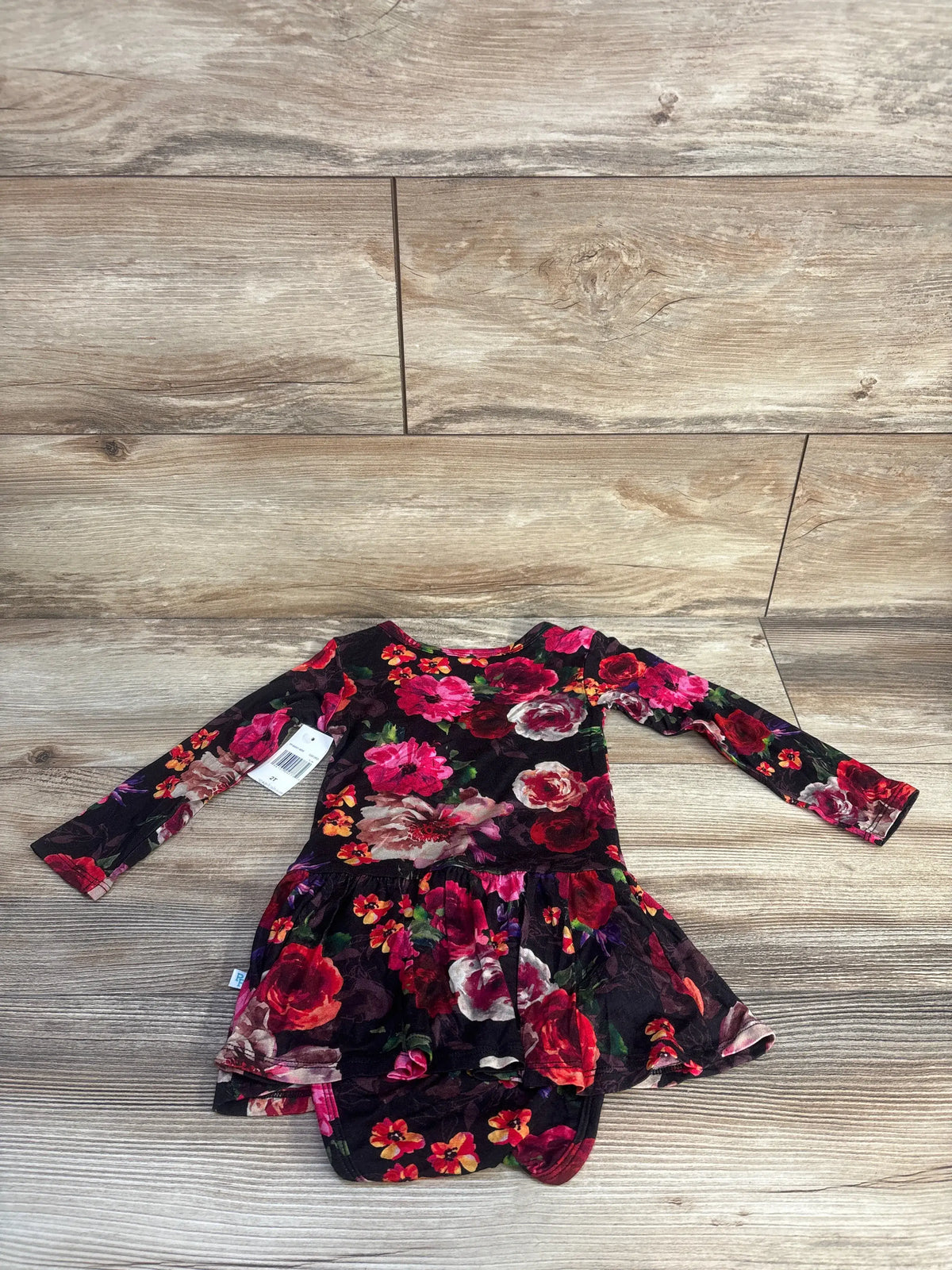 Top view of black twirl skirt bodysuit dress showcasing floral print and long sleeves on a wood floor
