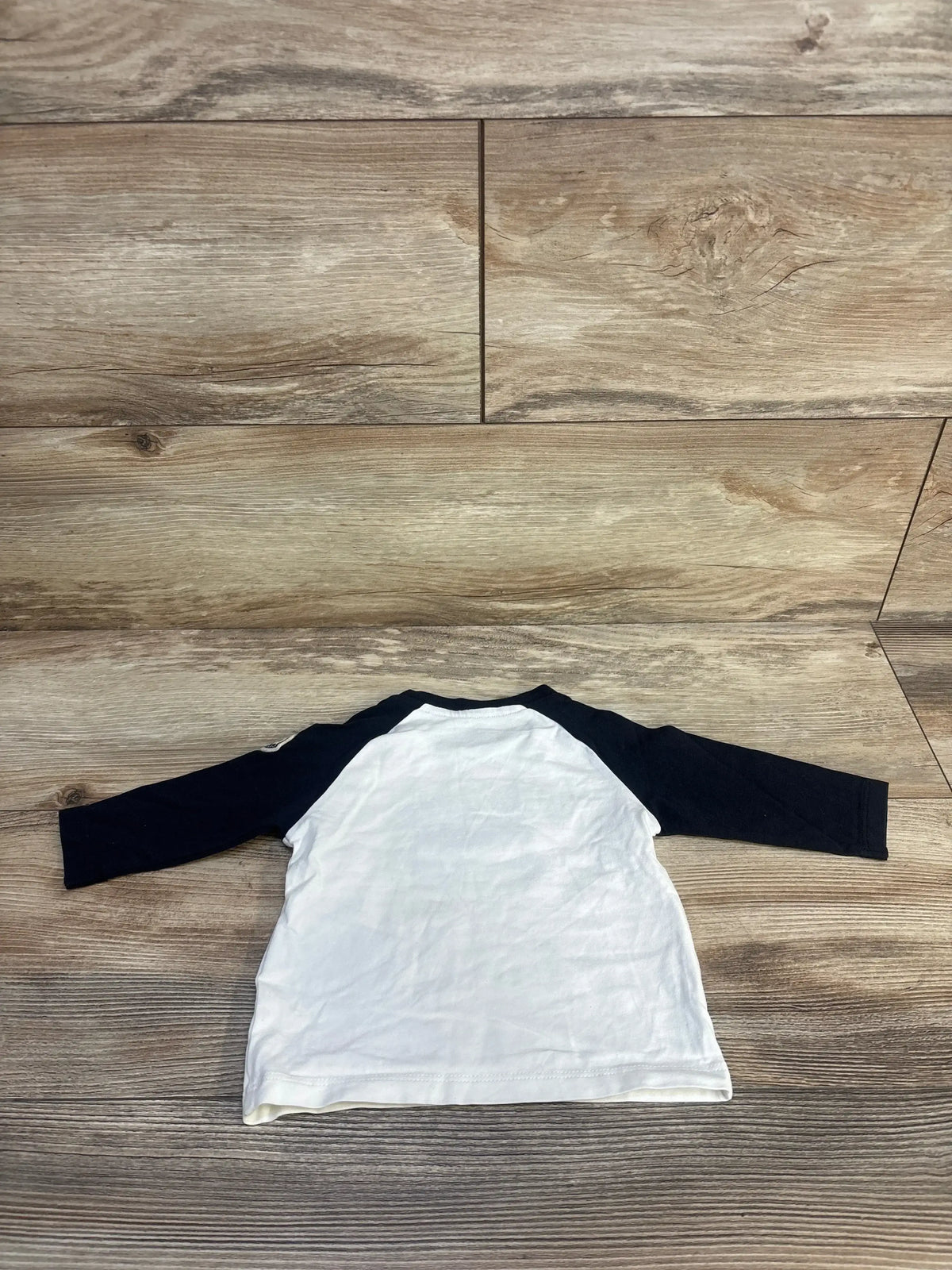 White and black long sleeve toddler shirt laid flat on wood floor