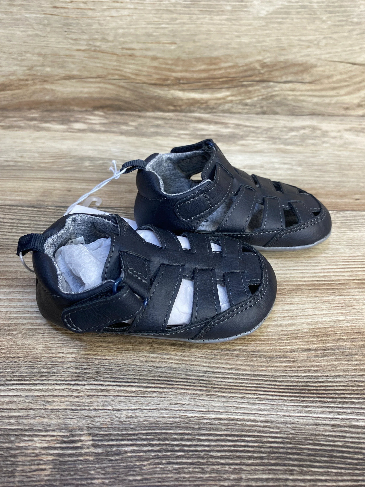 Angled side view of Just One You Harrison fisherman sandals in navy showing closed-toe and velcro strap on wood