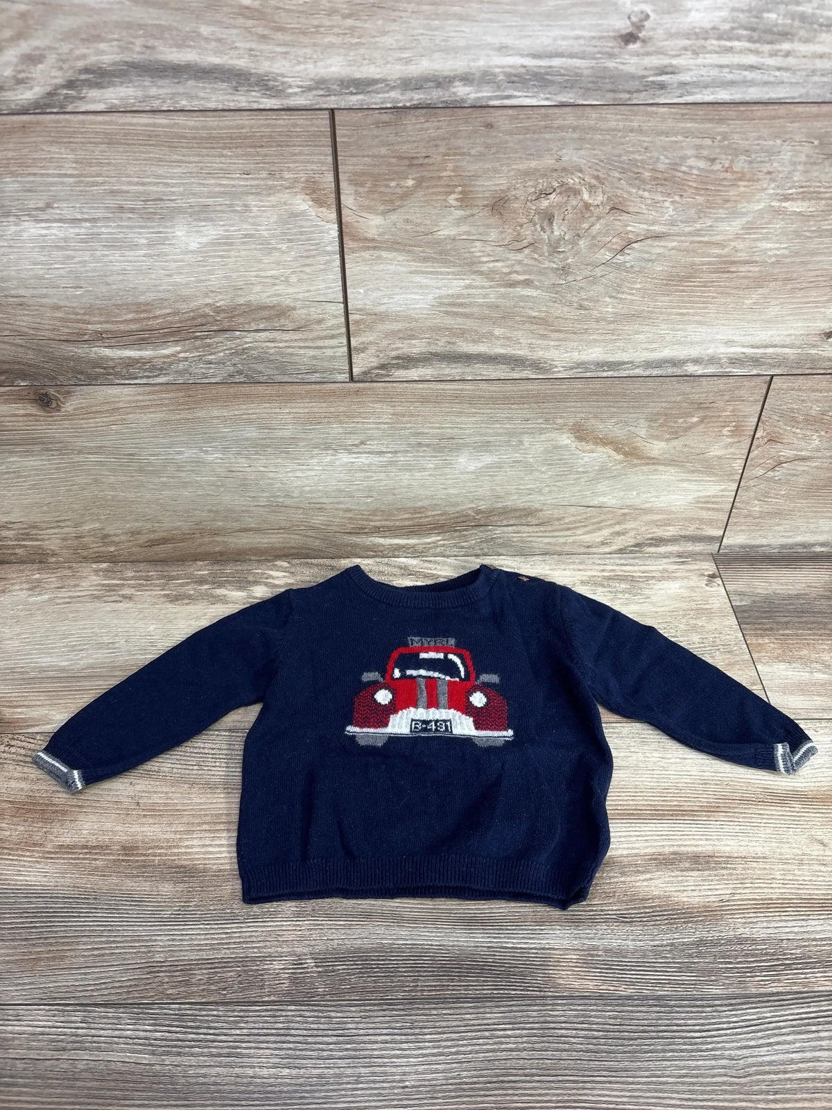 Navy blue toddler sweater with red car graphic, long sleeves, laid on wood floor