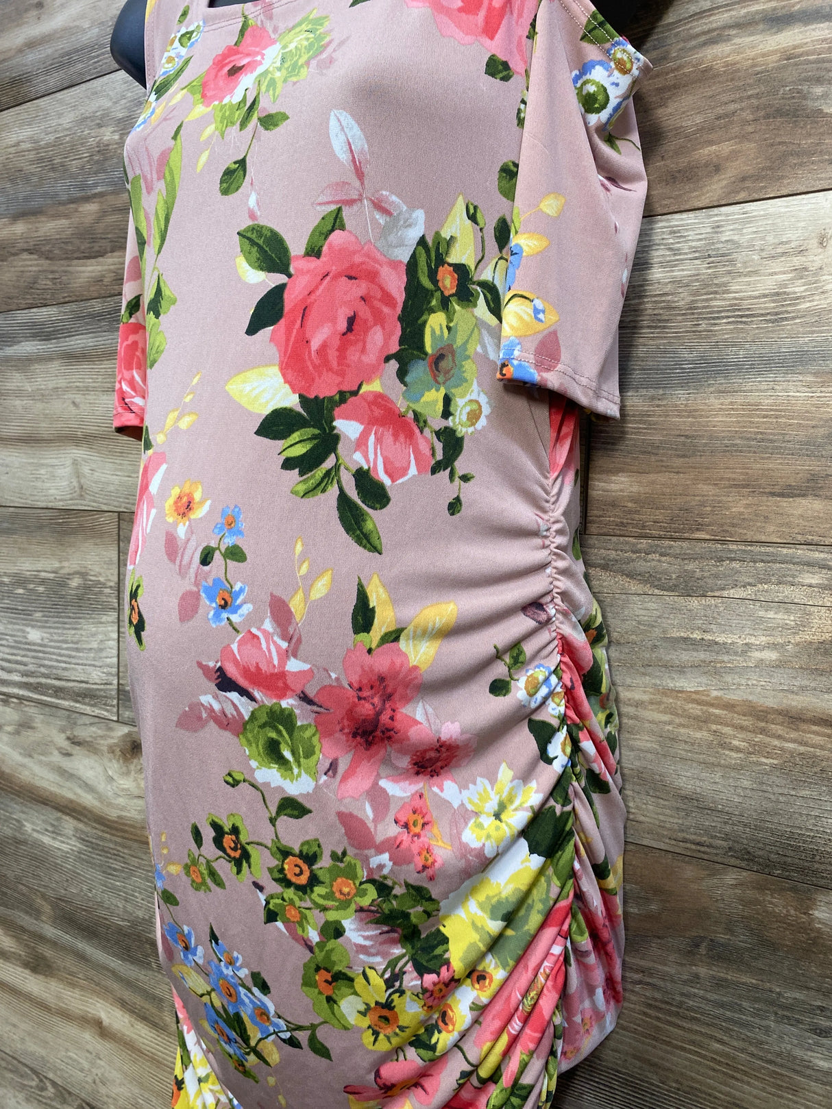 Pink ruched floral dress with rose and yellow flower print on mannequin, wood background