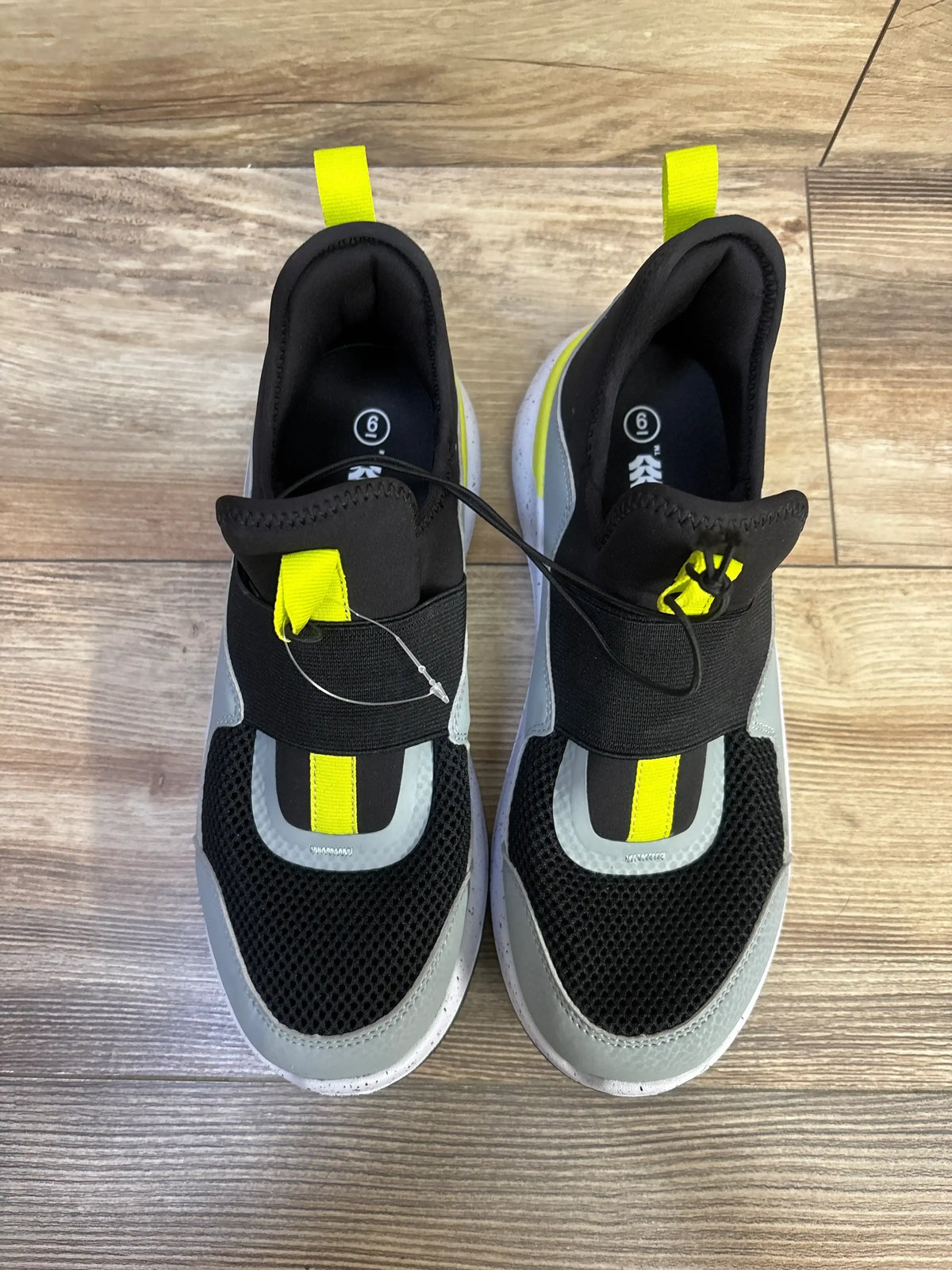 Top view of All In Motion slip-on youth sneakers size 6 with black mesh, grey panels and neon yellow tabs on wood floor