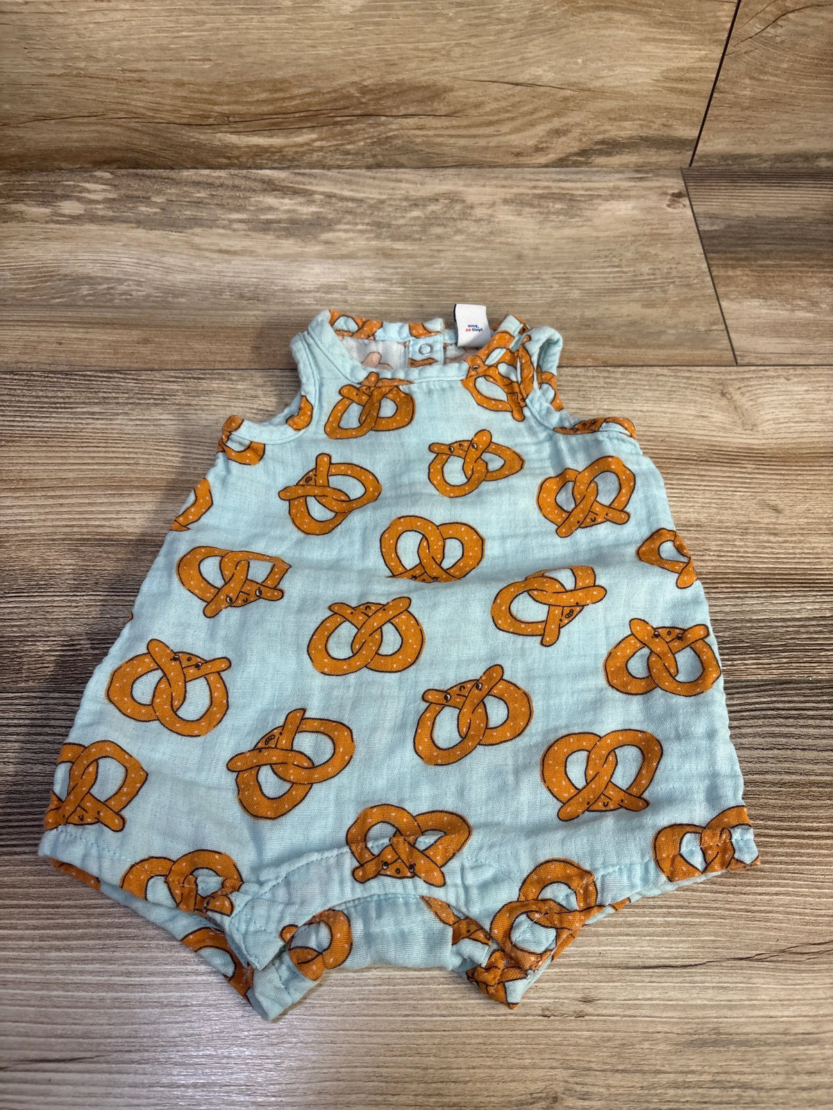 Flat lay of blue gauze newborn romper (0-3 mo) with orange pretzel print and ruffled shoulder straps on wood background