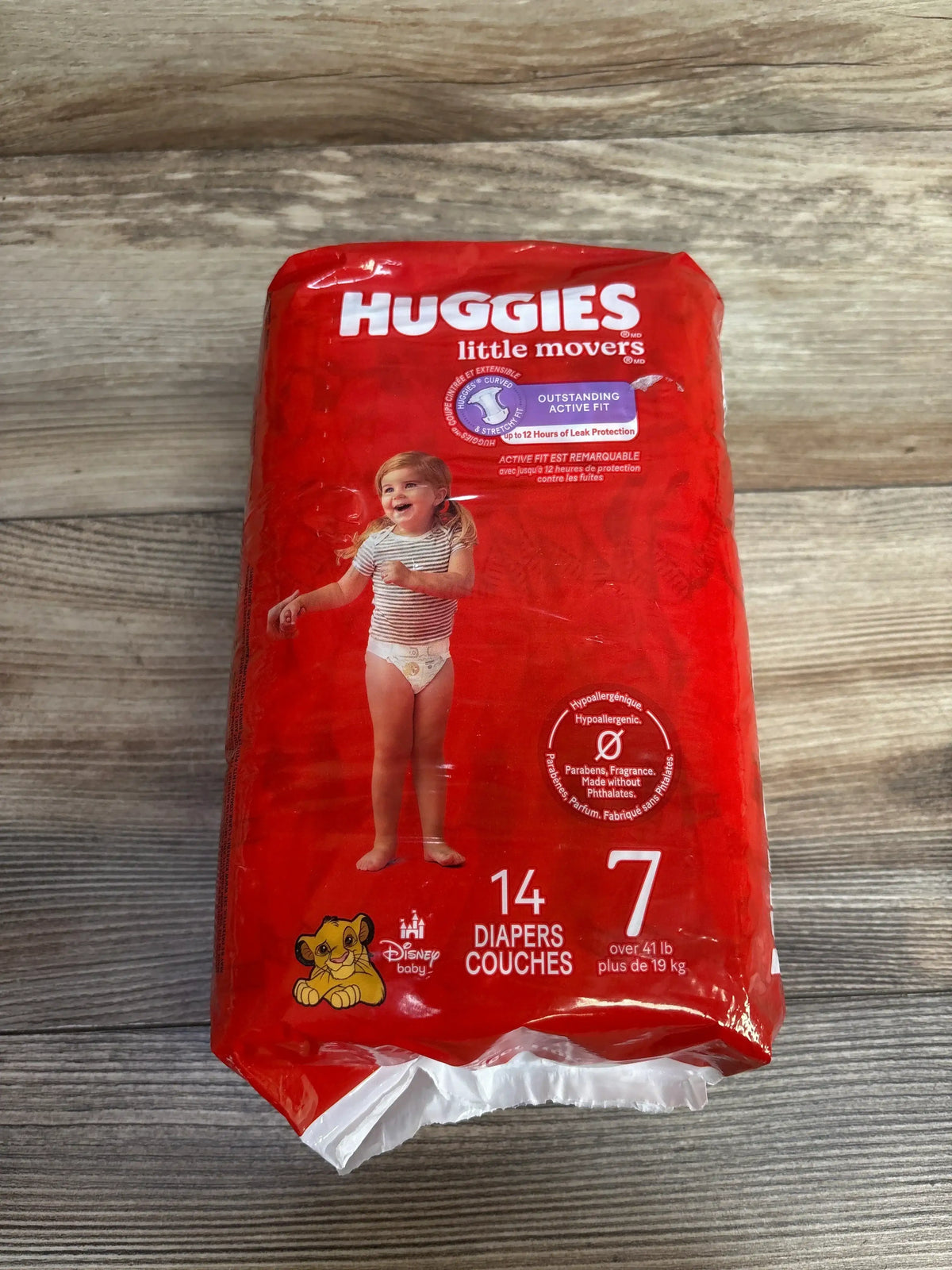 Front view of Huggies Little Movers size 7 diapers pack showcasing red packaging with Disney Lion King Simba graphic and 14 count on wood plank floor
