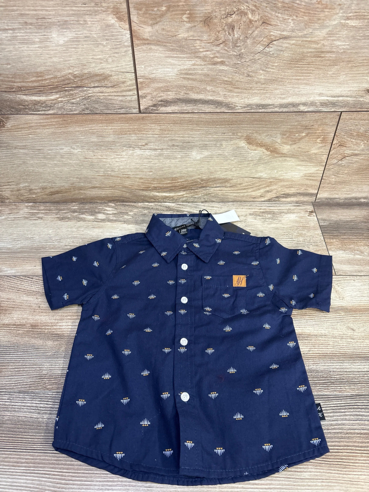 Top-down navy American Hawk button-up shirt (24M) with small white print, chest pocket with tan patch on wood floor