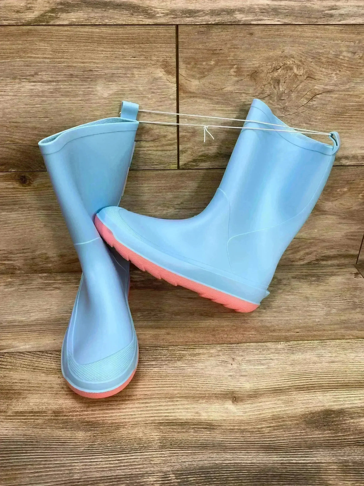 Angled side view of Cat & Jack Andy children’s slip-on rain boots in light blue with pink soles on a wood plank background