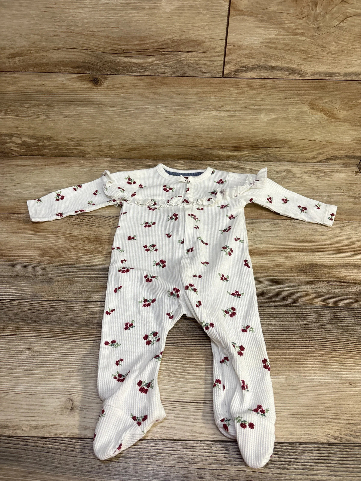 Front flat lay of white thermal sleeper with red floral print, ruffle chest, ribbed texture and footed legs on wood