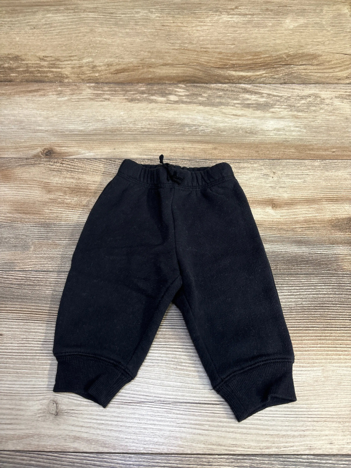Flat lay of baby black Jumping Beans drawstring joggers size 3M showing elastic drawstring waist and ribbed ankle cuffs on light wood background