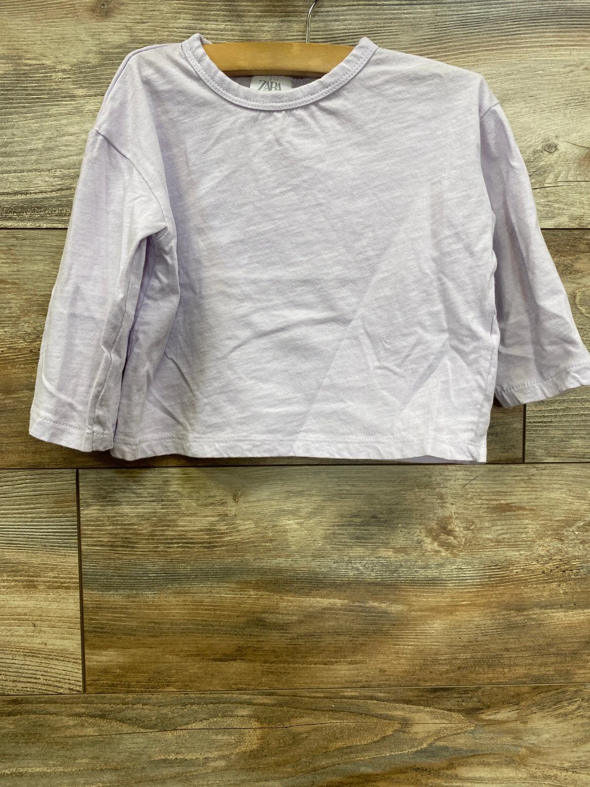 Light purple long sleeve kids shirt on wooden hanger against wood background