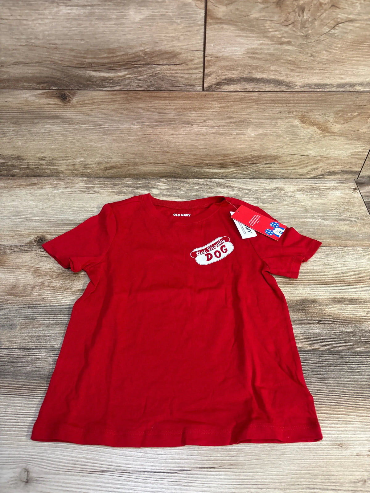 Flat lay of red Old Navy x Disney toddler T-shirt with Hot Diggity Dog chest graphic and size tag on wood background