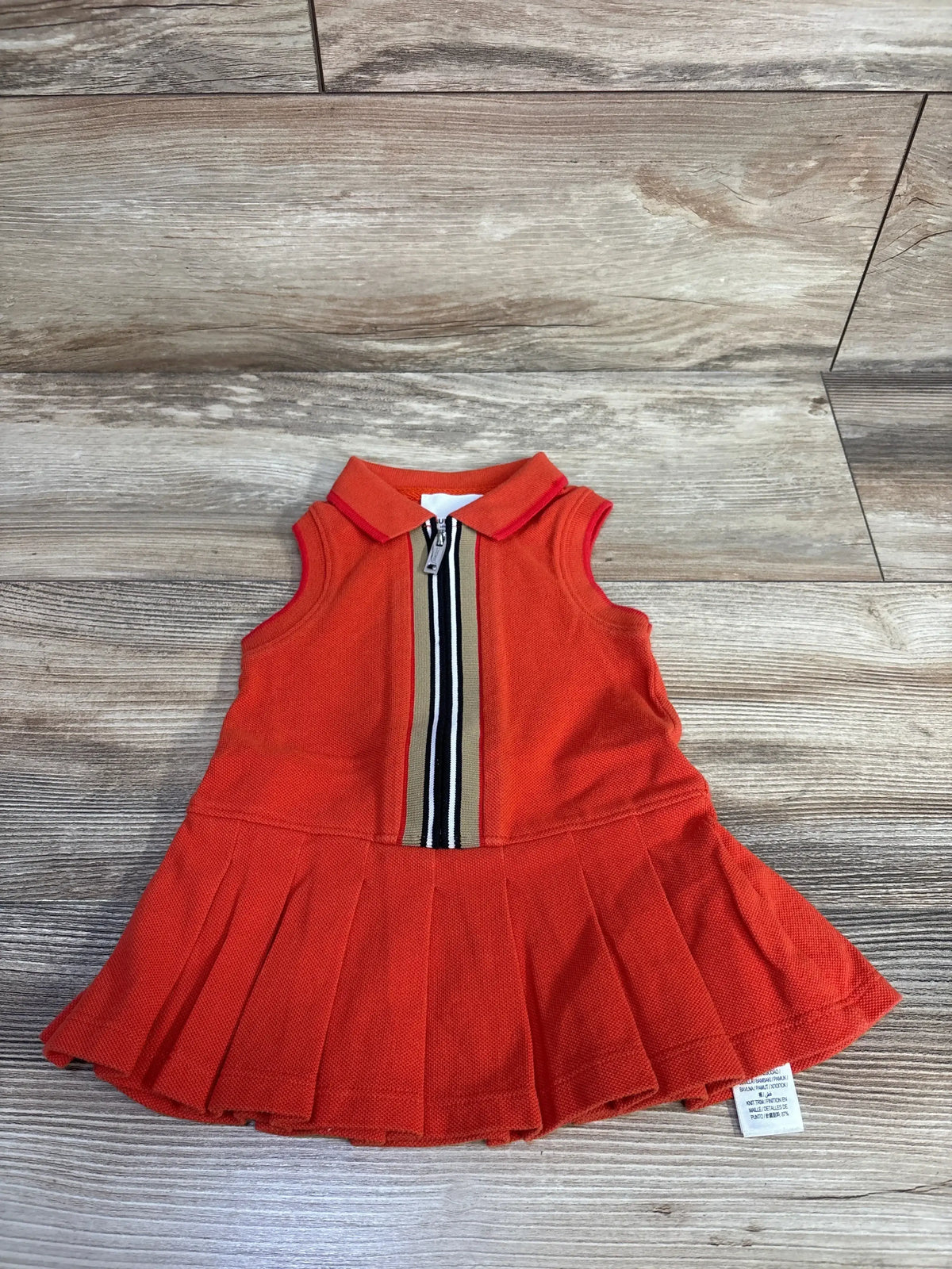 Flat lay of Burberry polo dress 6M showcasing front zipper with beige black white stripe and pleated skirt on wood floor