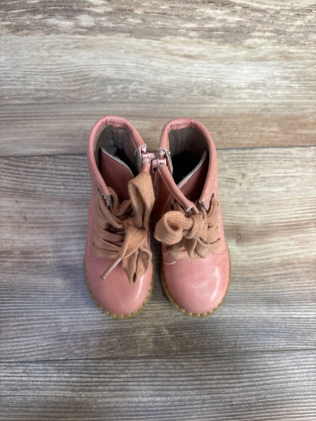Pair of pink toddler boots with large fabric bows on wooden floor