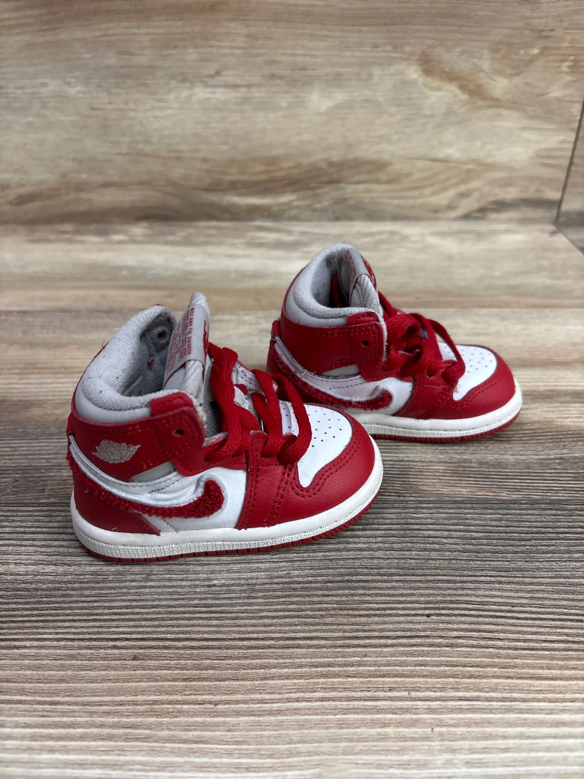 Three quarter view of Air Jordan 1 High Retro OG Newstalgia Chenille sneakers showcasing chenille Swooshes on wood grain