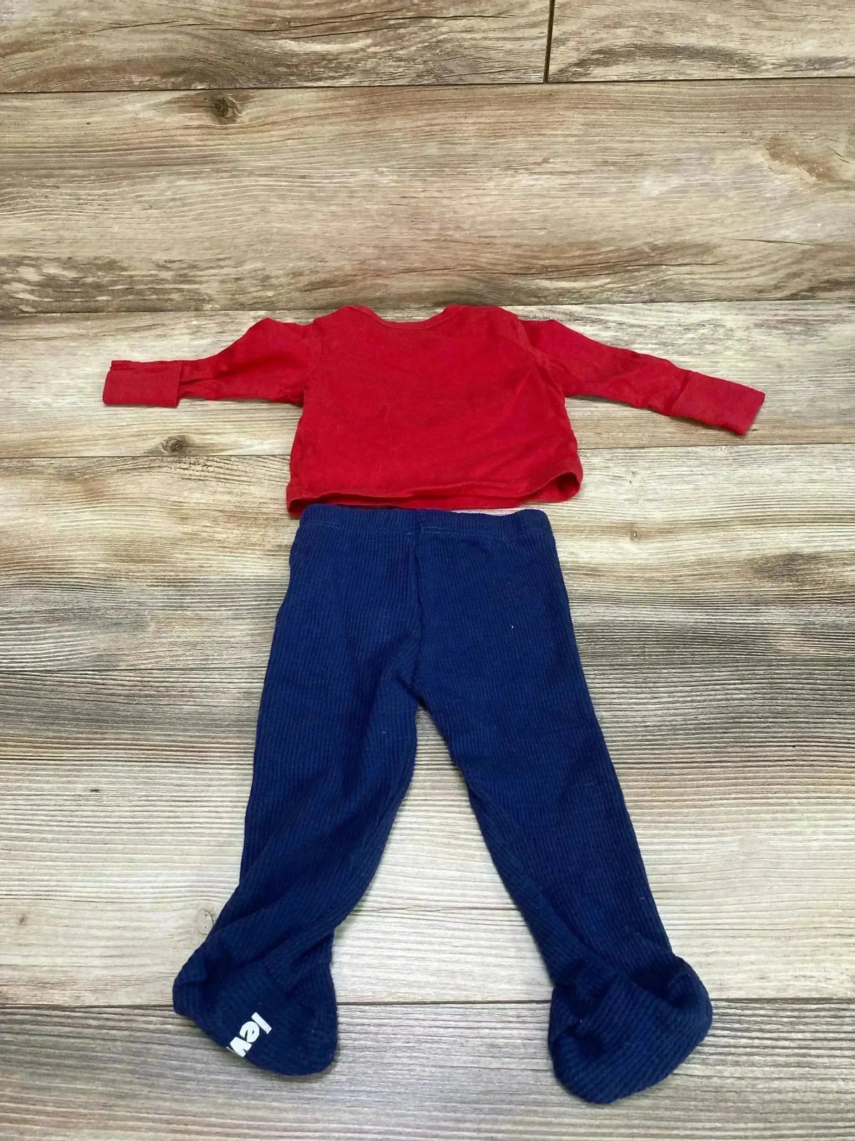 Flat lay of Levis 2-piece infant set showing red long-sleeve shirt and navy footed pants size 3 months on wood floor