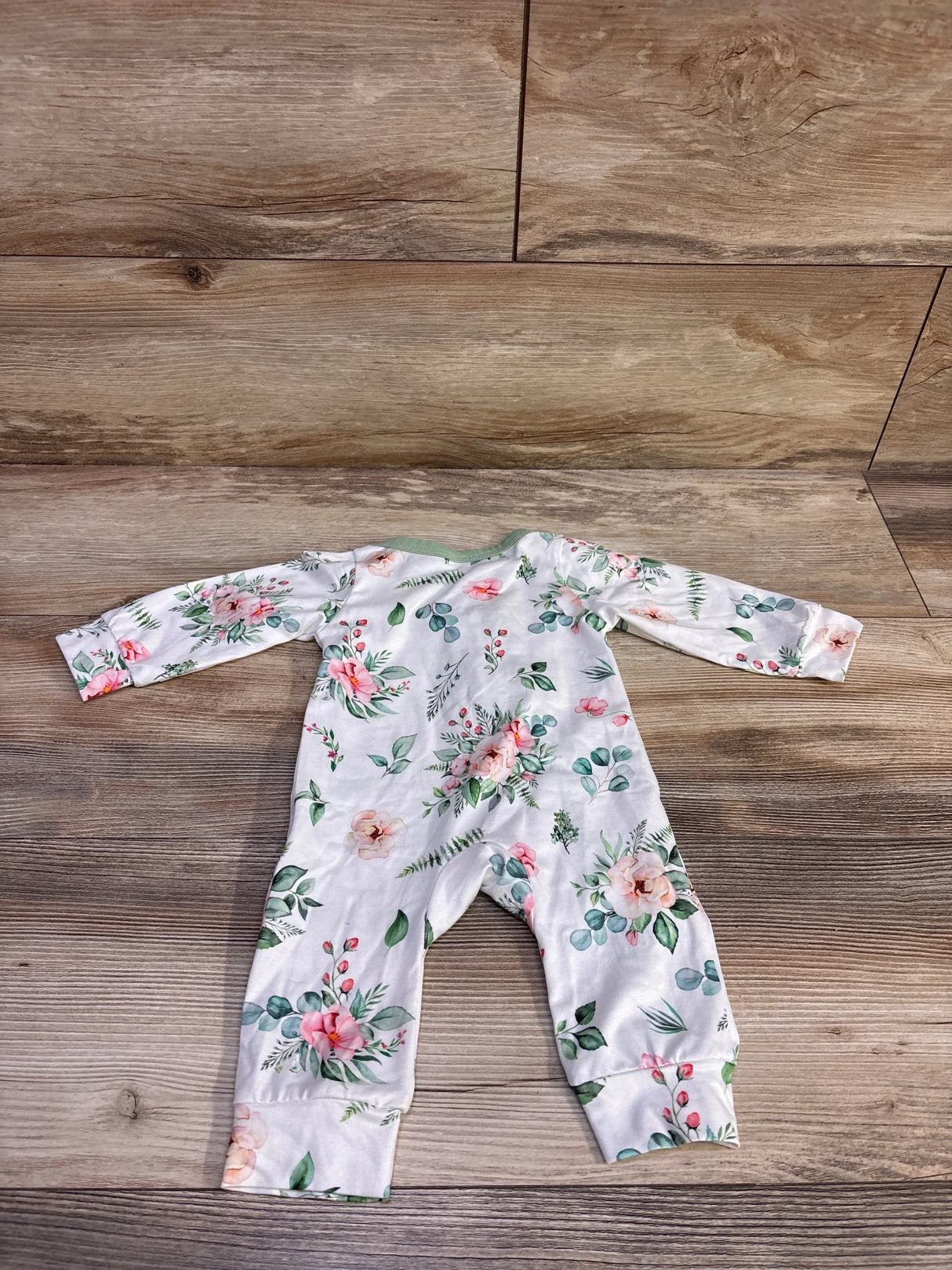 Flat lay of newborn white floral coverall with mint trim showing long sleeves and fold-over cuffs on wood background