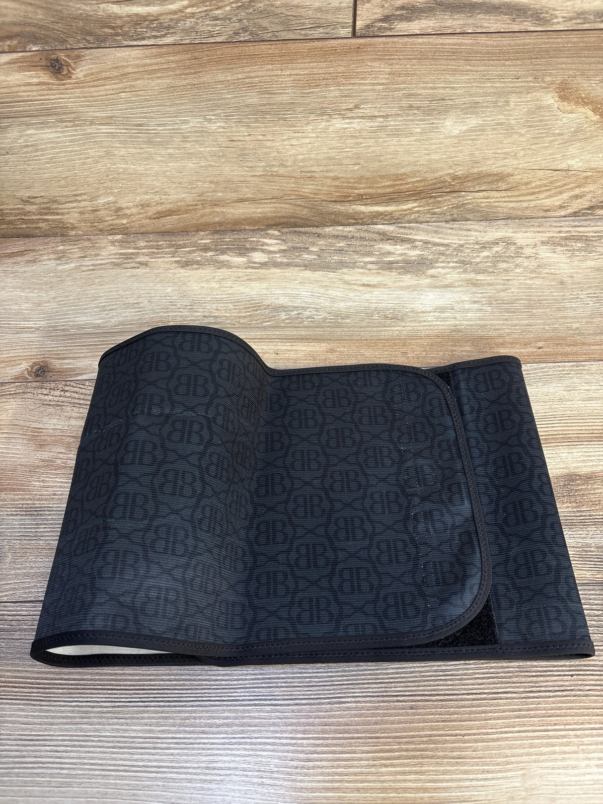 Black patterned postpartum belly wrap with Velcro closure on wood floor