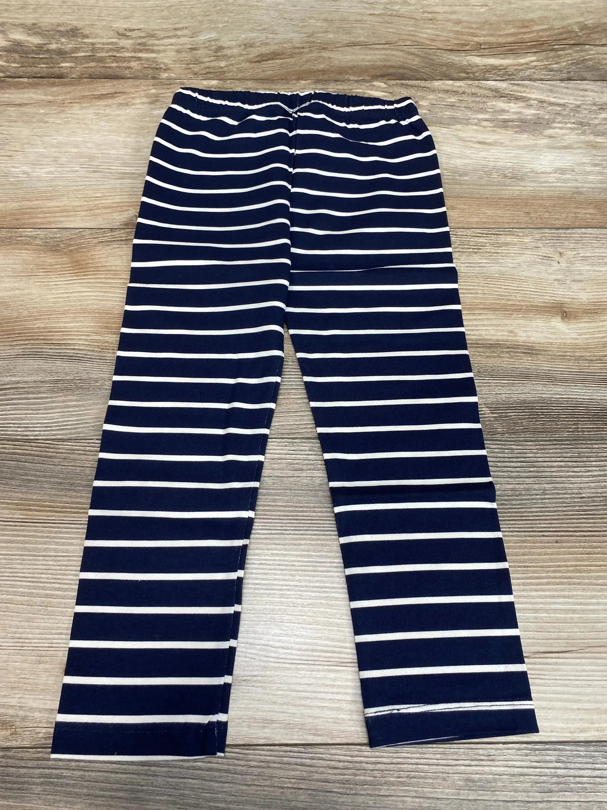 Flat lay of Baby Gap navy and white striped toddler leggings size 3T showing elastic waistband and straight legs on light wood floor background