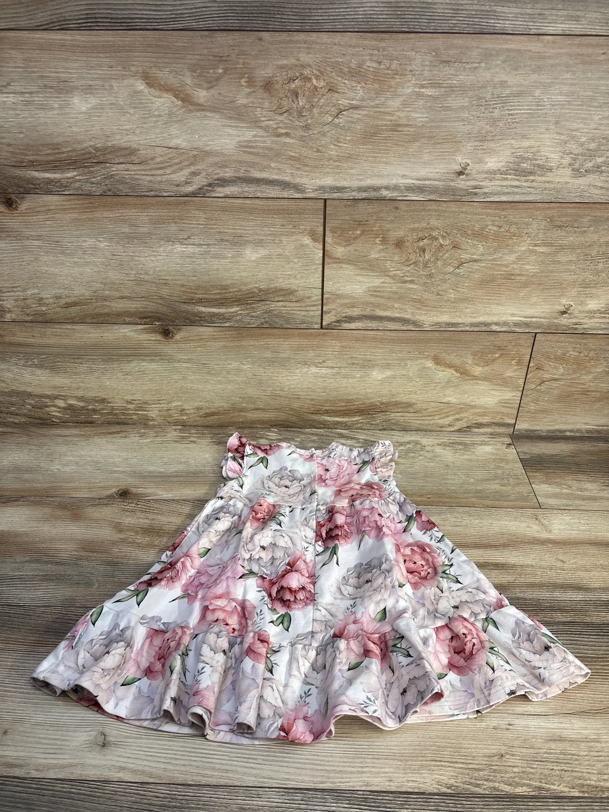 Flat lay of Sofia Mila pink floral sleeveless dress showcasing its ruffled hem on a wood floor