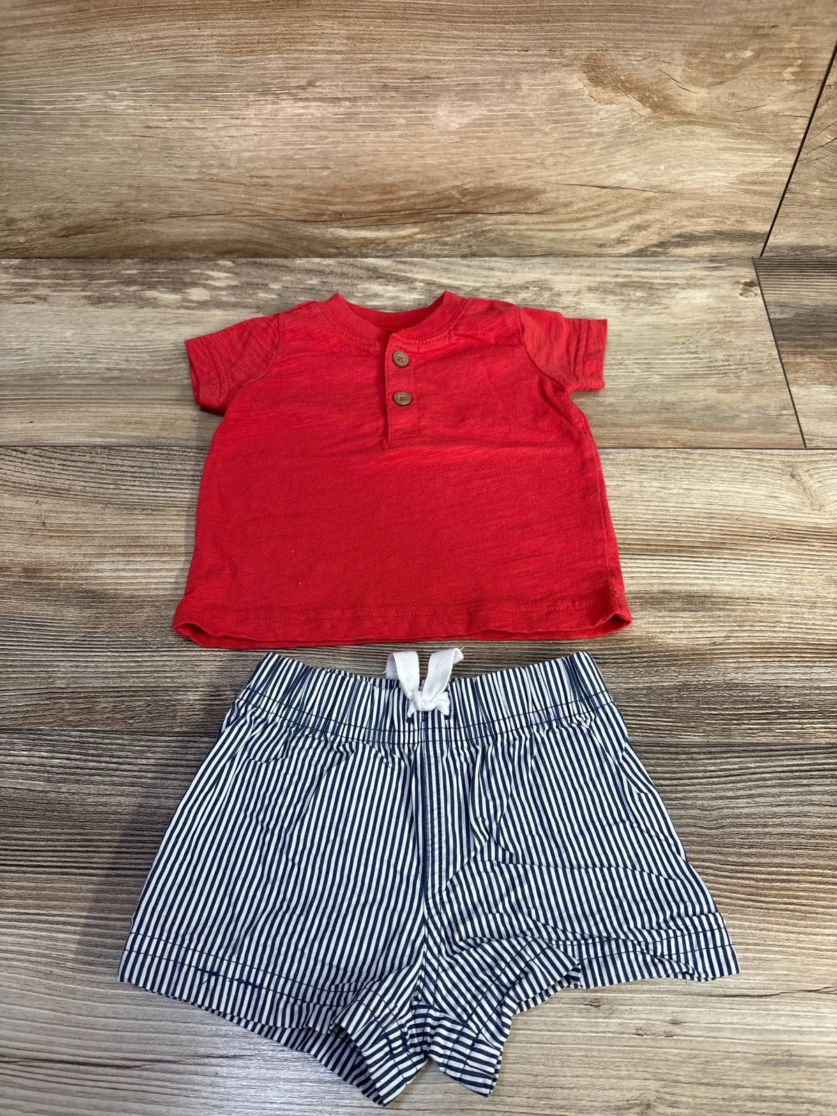 Front view of Just One You shirt and shorts set with a red short sleeve shirt and navy striped shorts on wood