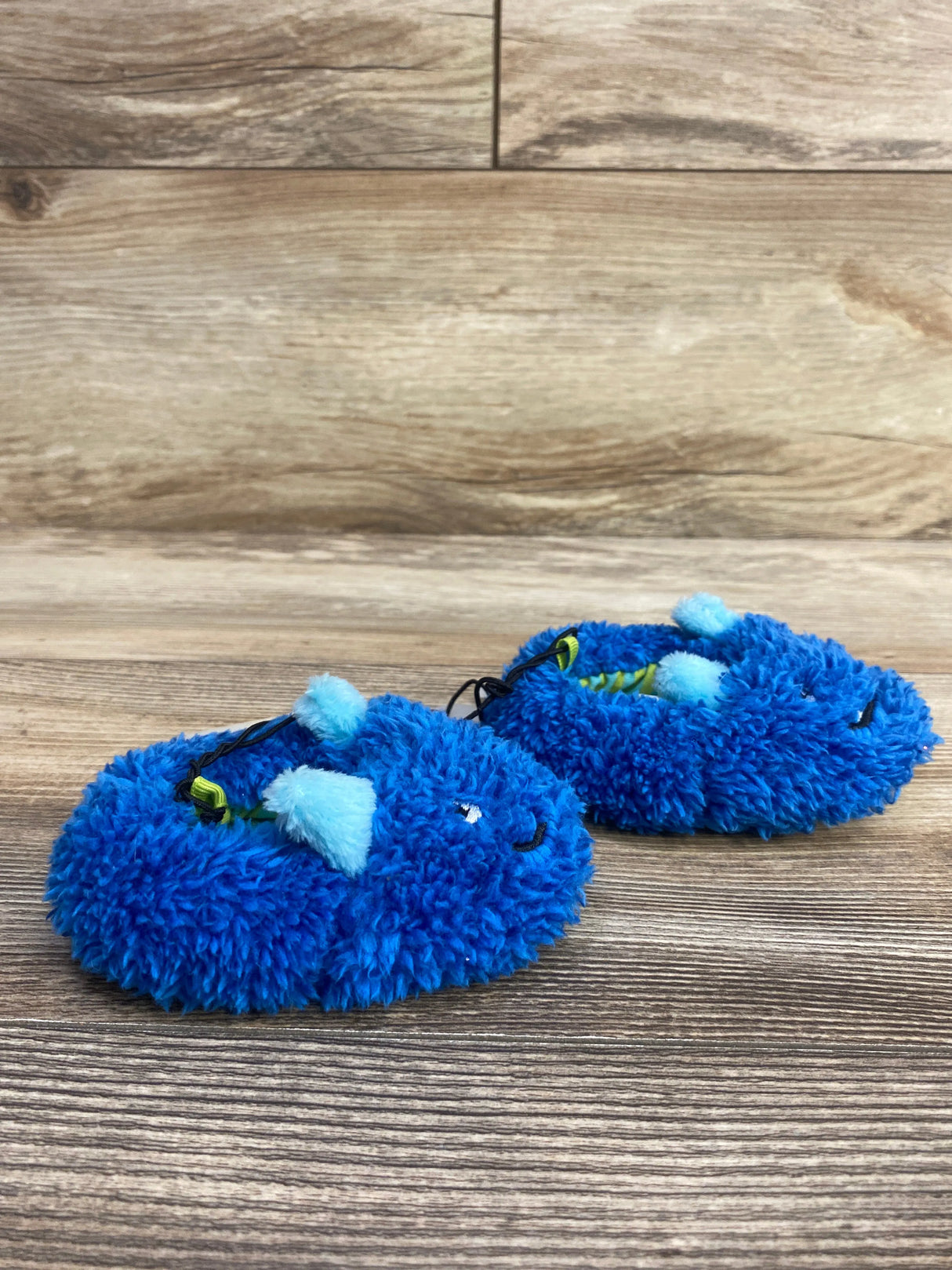Pair of fuzzy blue baby slippers with ears and faces on wooden surface
