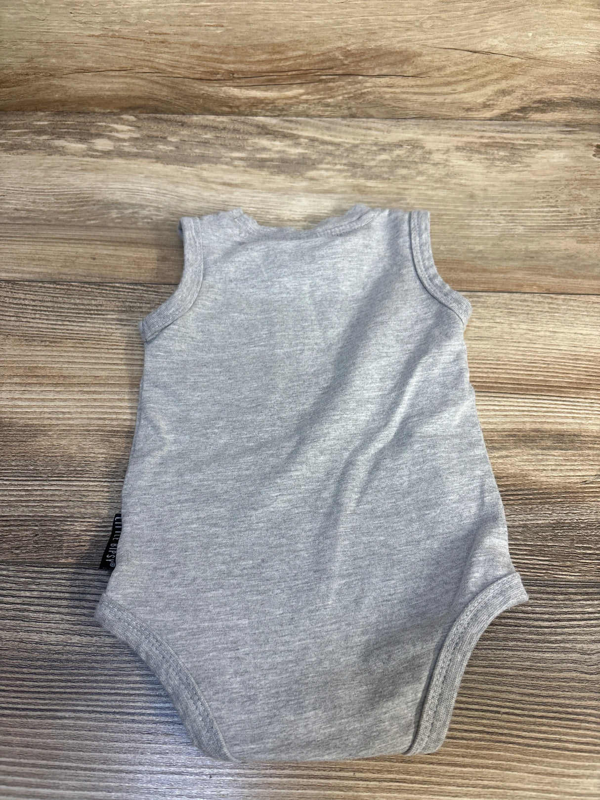 Gray sleeveless baby bodysuit on wood background, gently used kids clothing