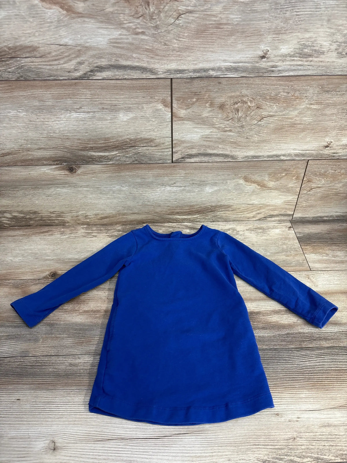 Long-sleeve solid blue toddler dress laid flat on rustic wooden floor
