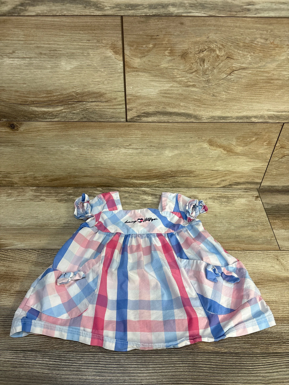 Baby dress with pink and blue plaid pattern, short sleeves, and bow accents on wood floor