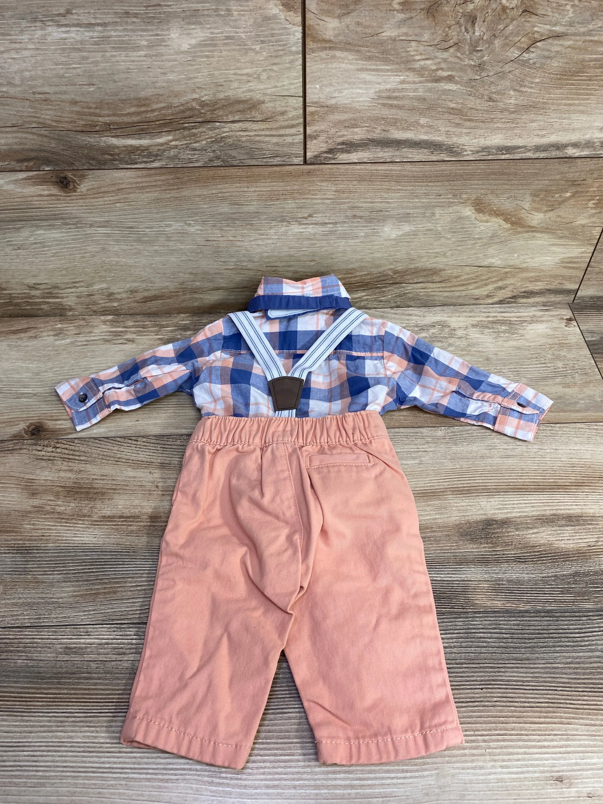 Baby boy plaid shirt with suspenders and peach pants set on wood background