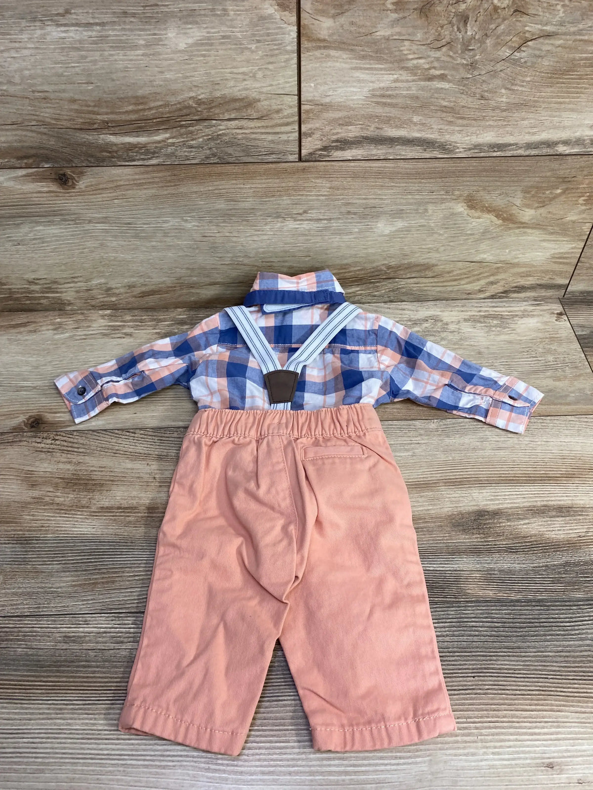 Baby boy plaid shirt with suspenders and peach pants set on wood background