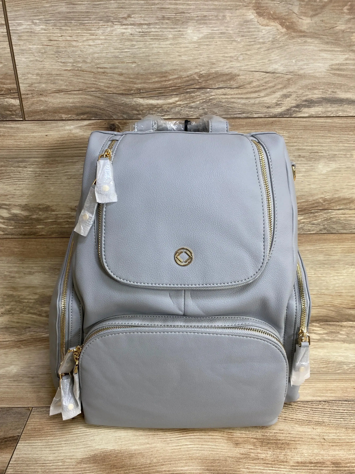 Light gray diaper bag backpack with multiple zipper pockets on wood floor