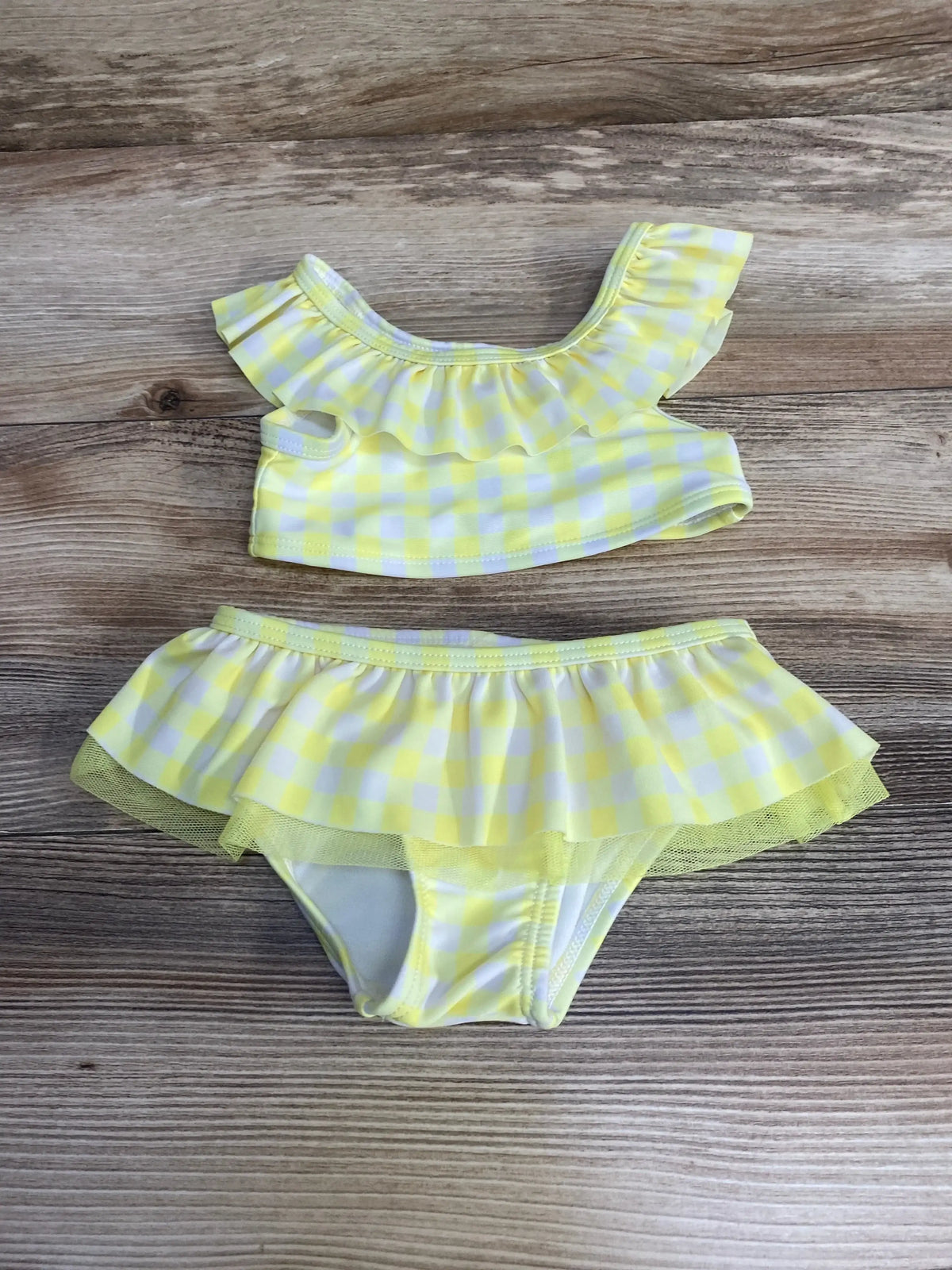 Flat lay of yellow gingham 2-piece baby swimsuit (12M) showing ruffled shoulder top and skirted bottoms on wood background