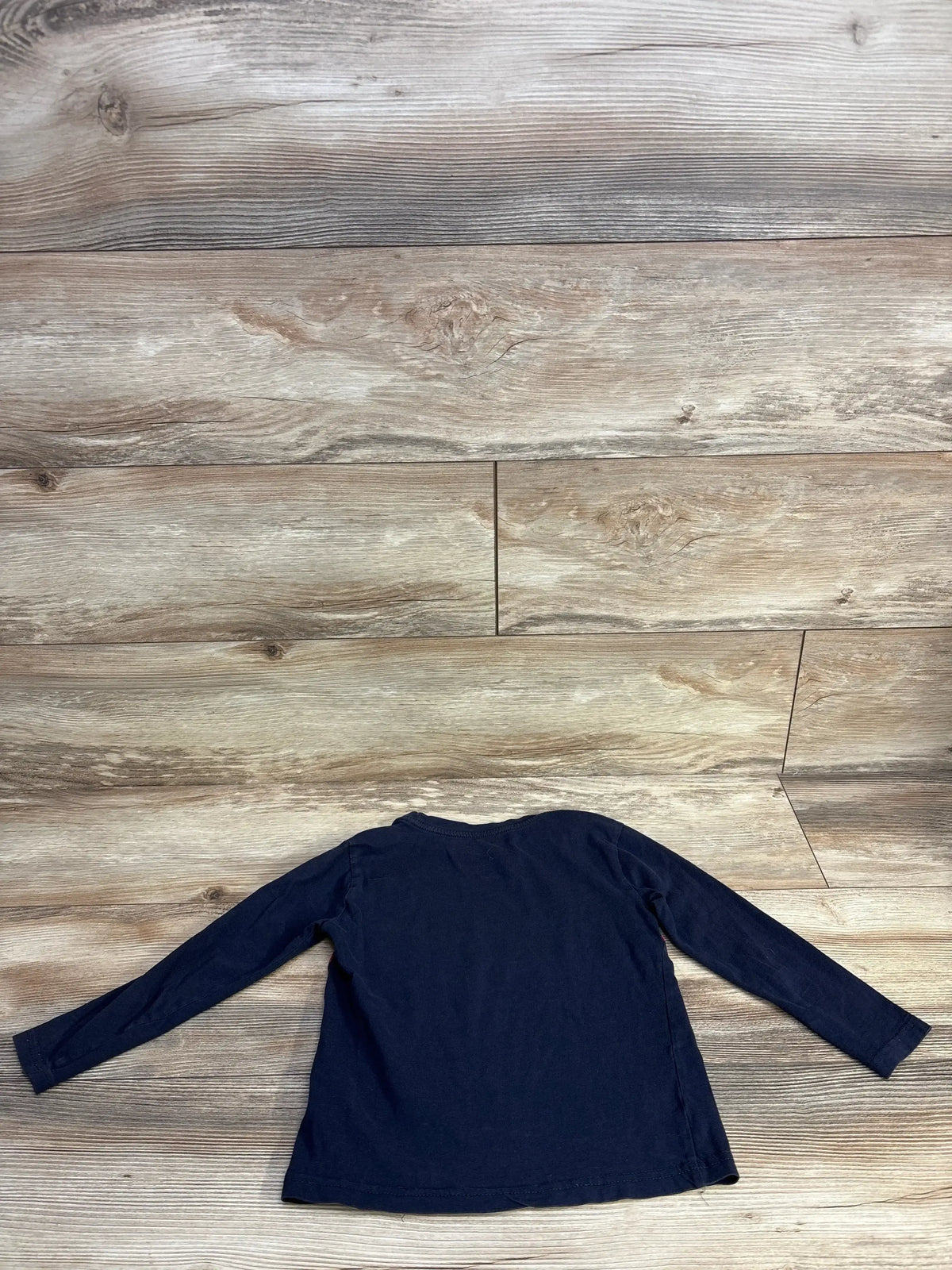 Back view of Tommy Hilfiger 4T navy long-sleeve shirt showing plain back and long sleeves on wood plank background