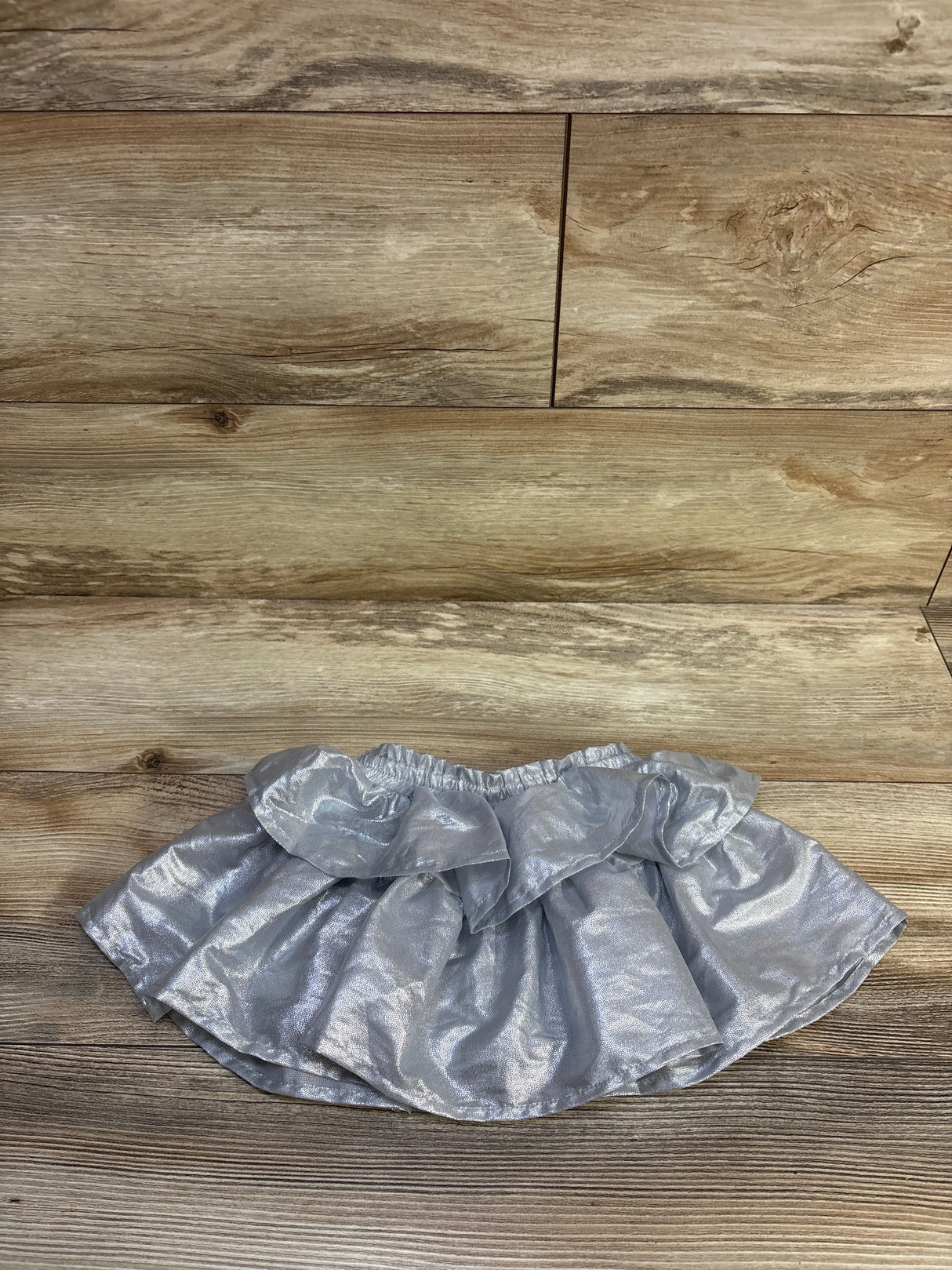 Flat lay of metallic silver toddler skort with ruffled layers and elastic waist on wood floor background