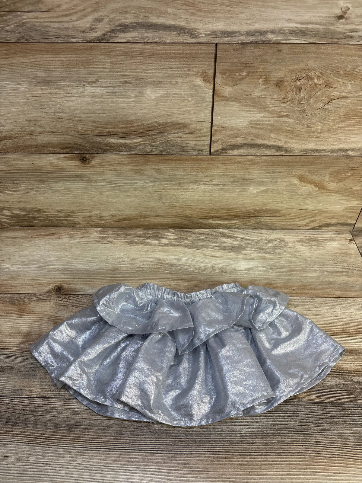 Flat lay of metallic silver toddler skort with ruffled layers and elastic waist on wood floor background