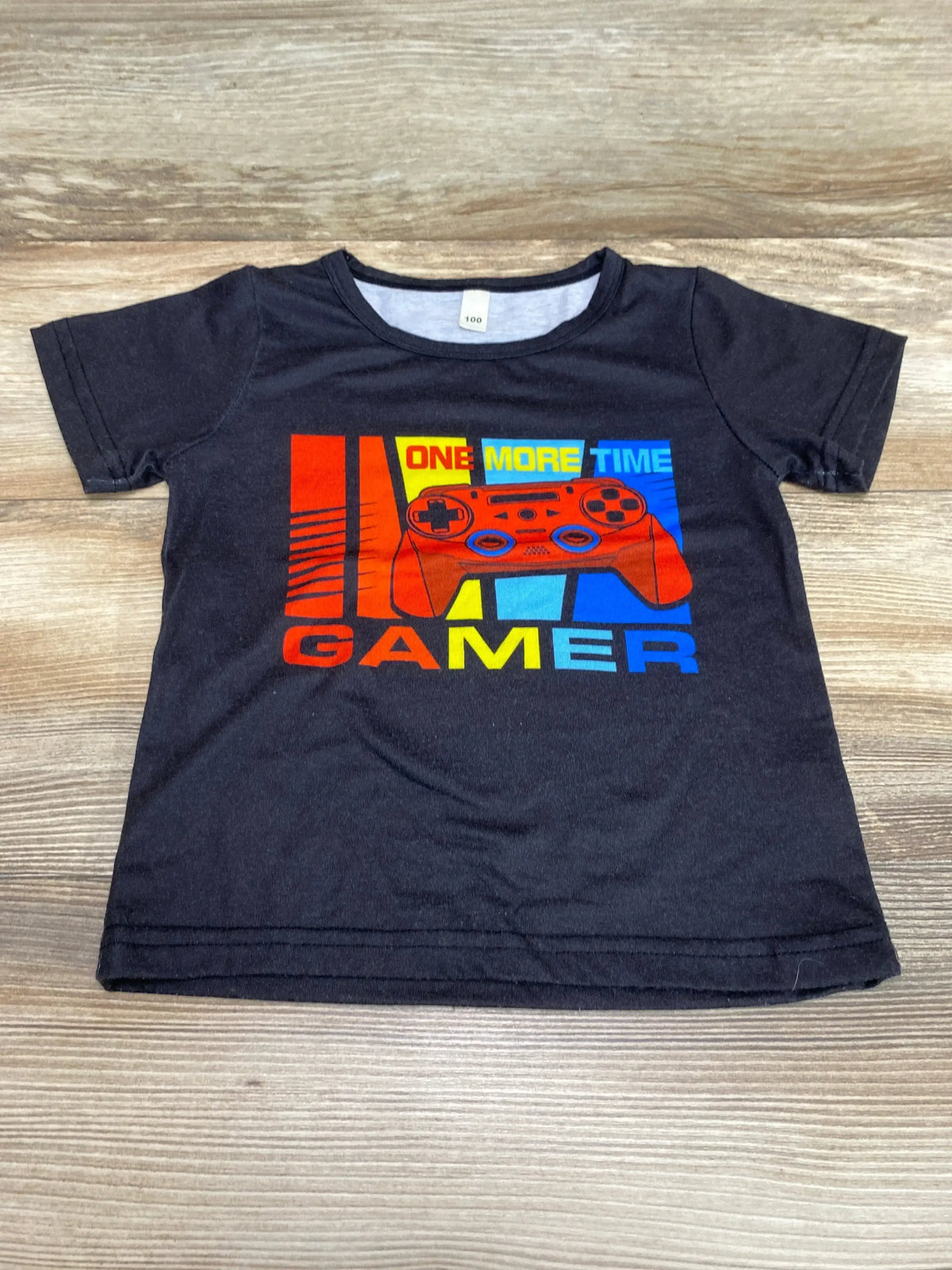 Flat-lay of black toddler t-shirt (2T) showing red game controller graphic and the words ONE MORE TIME GAMER on a wood surface