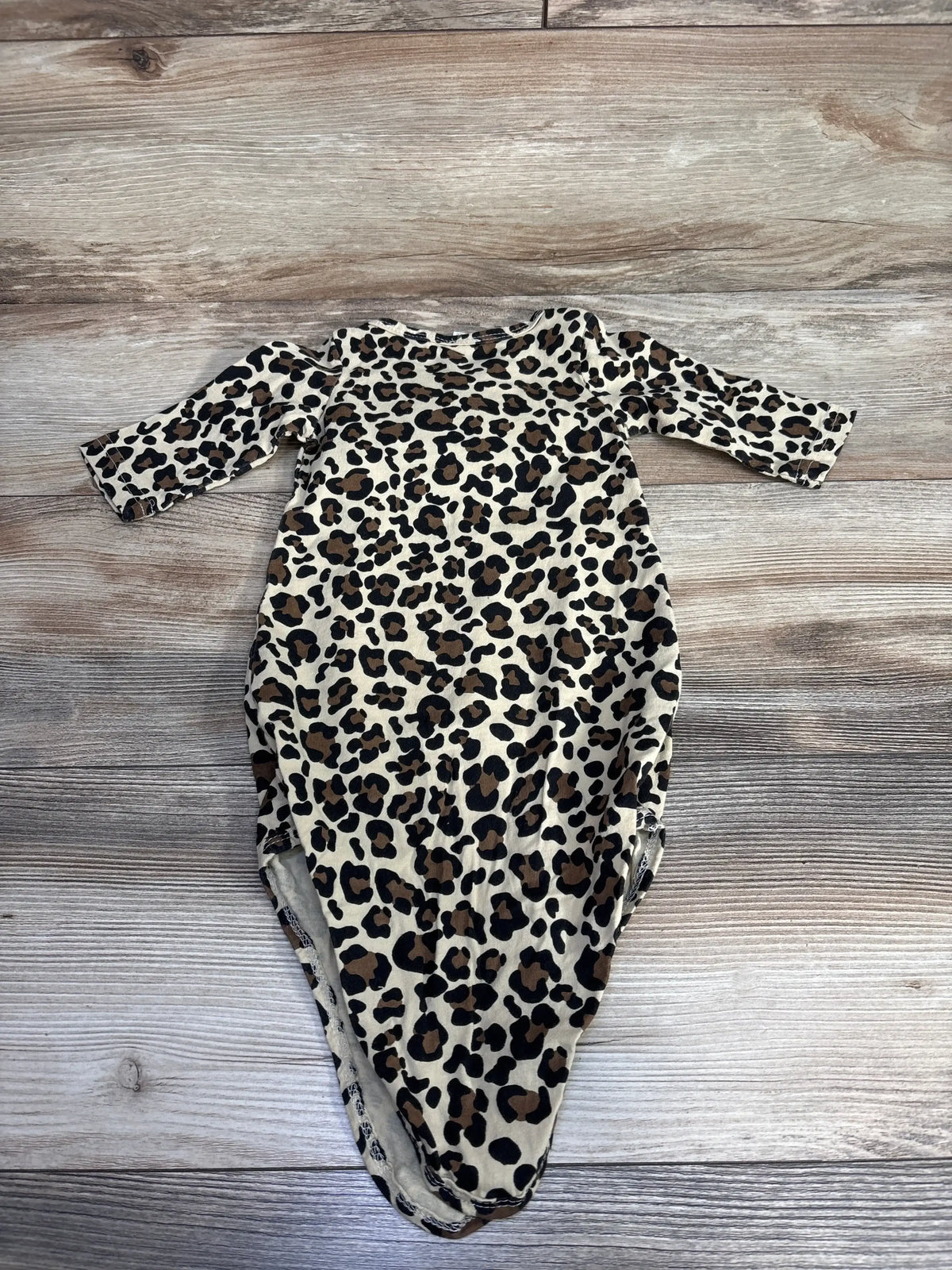 Front view of leopard print knotted baby gown with long sleeves showing knotted bottom on wood background