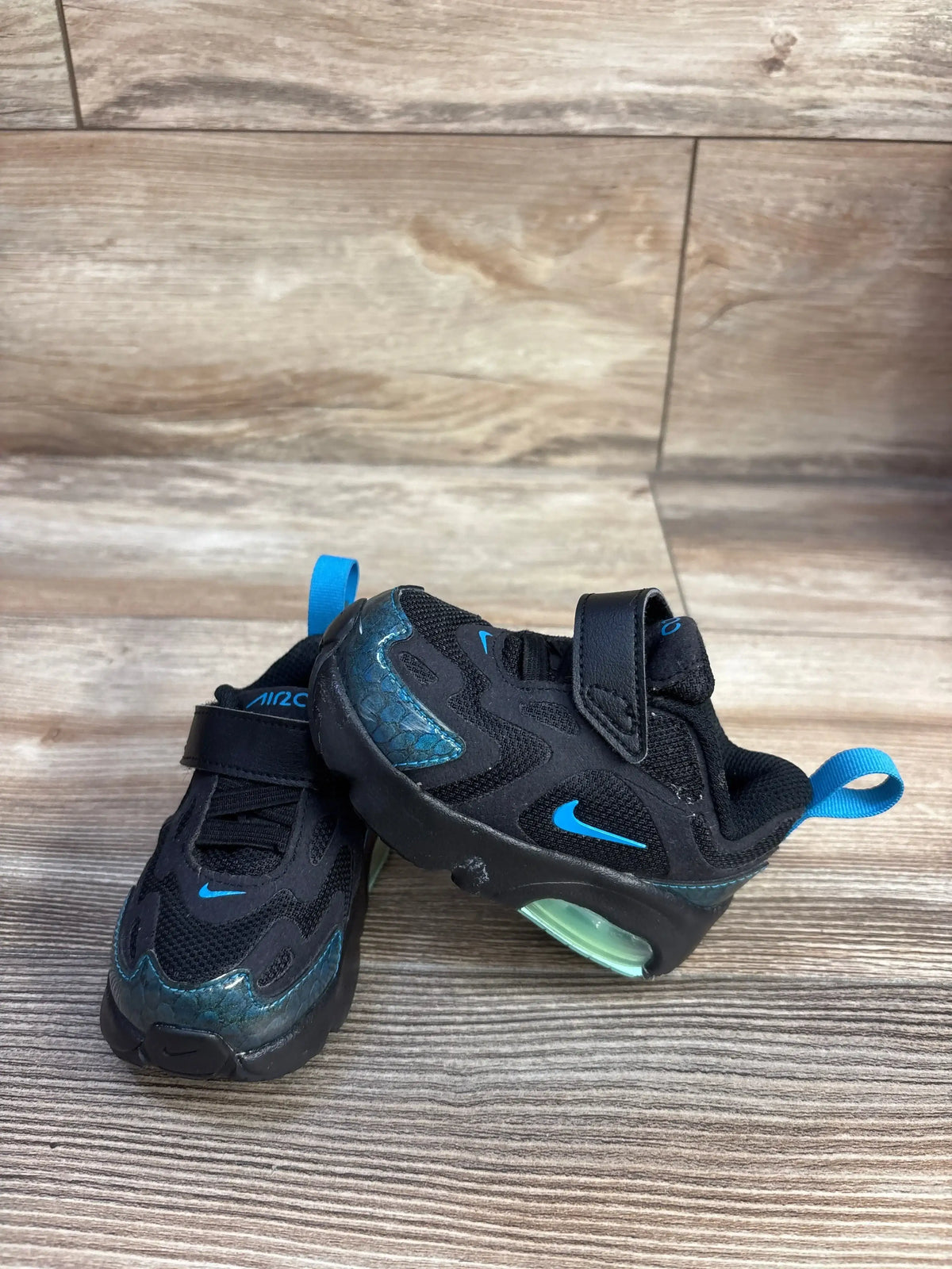 Three-quarter view of toddler Nike Air Max 200 Black Aurora sneaker showcasing black mesh, blue accents, and visible green Air unit on wood floor