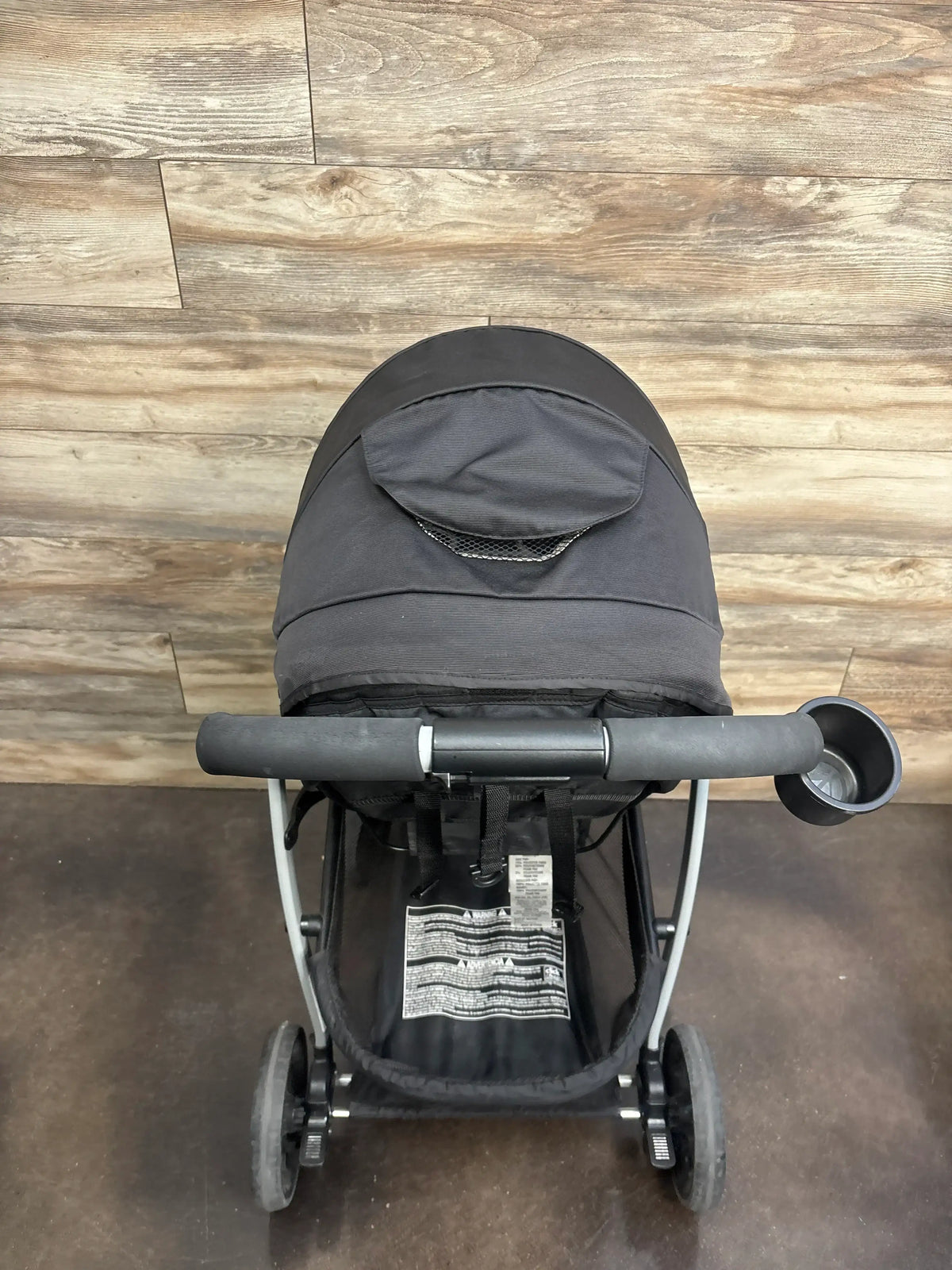 Front view of Graco Modes Pramette stroller showcasing black canopy and cup holder with wood-look floor background