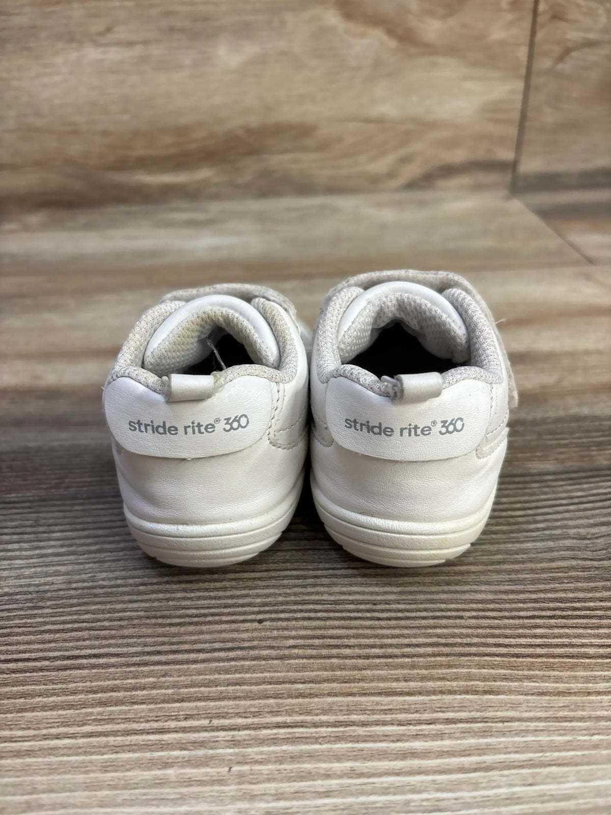Rear view of a pair of white Stride Rite Taye 2.0 sneakers showing padded collars and 360 branding on a wood floor