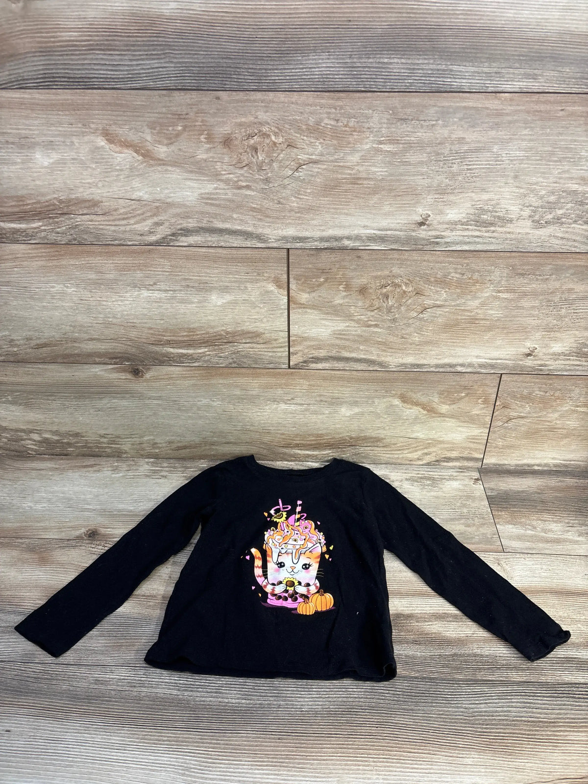 Front view of Children’s Place black fall cat shirt showcasing a cat and pumpkin graphic on a wood-patterned floor