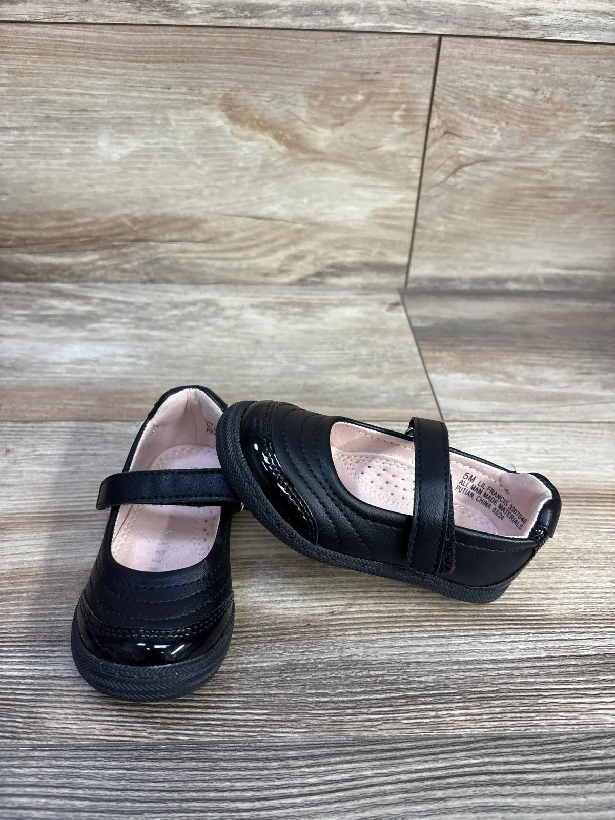Angled view of Kelly and Kate Francis black Mary Jane flats showing strap, patent toe, pink cushioned insole on wood floor