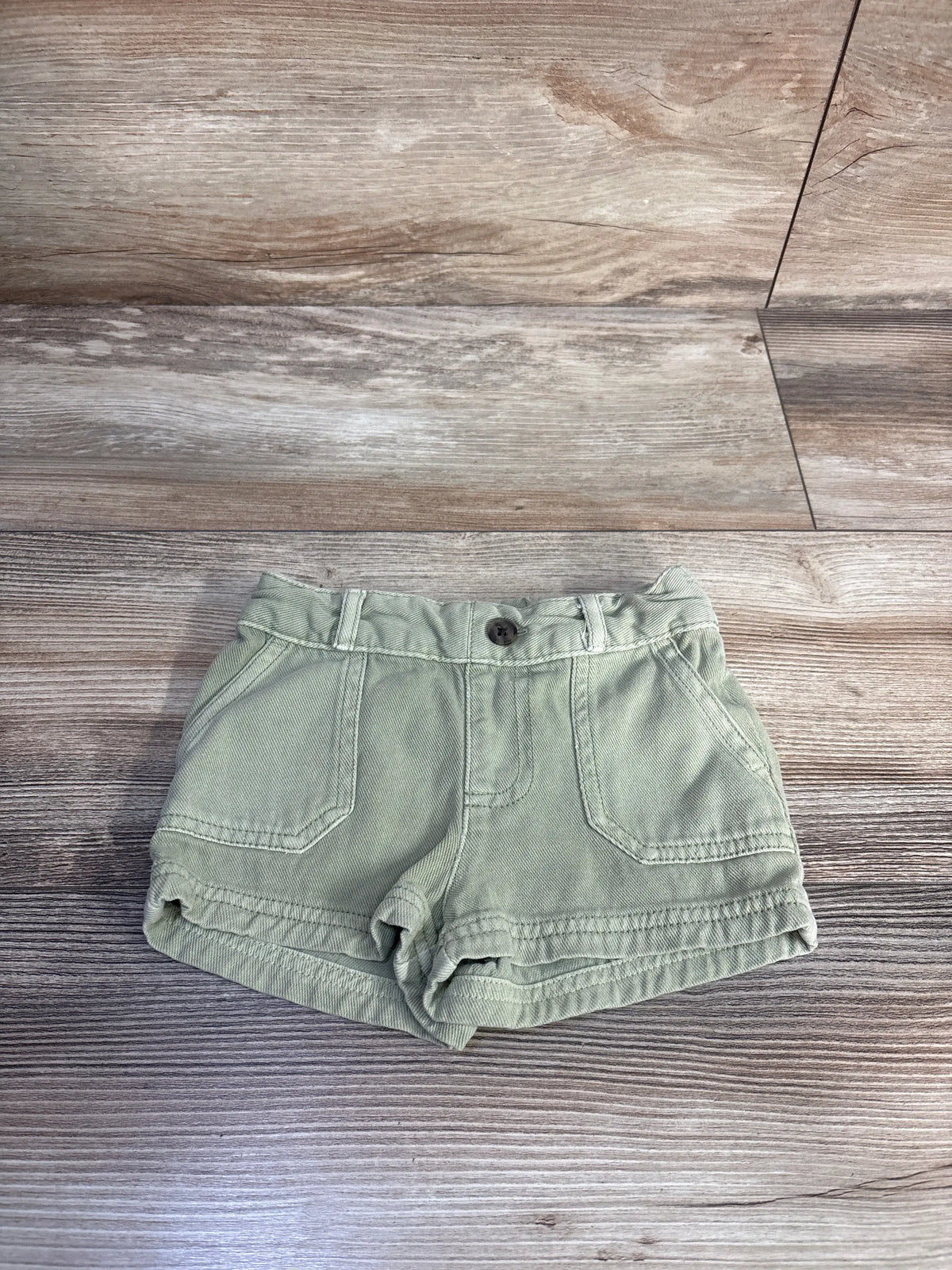 Front view of Cat & Jack green toddler shorts showcasing front pockets, button closure, and belt loops on a wood grain background