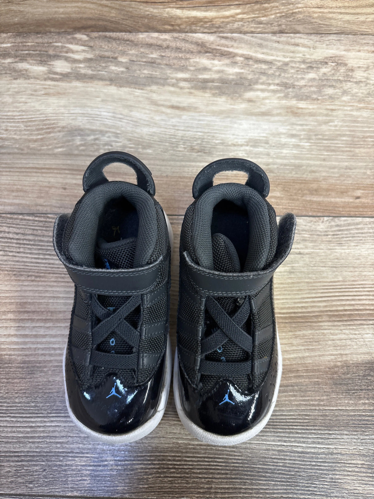 Black toddler Air Jordan sneakers with white soles on wood floor